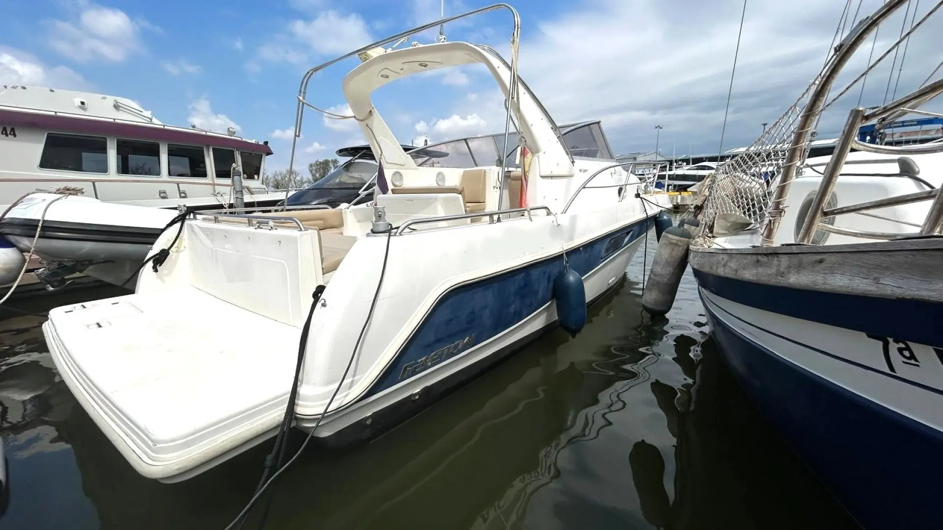 Faeton 980 Sport — Bateau à moteur blanc et bleu amarré dans un port, vu de trois quarts arrière.