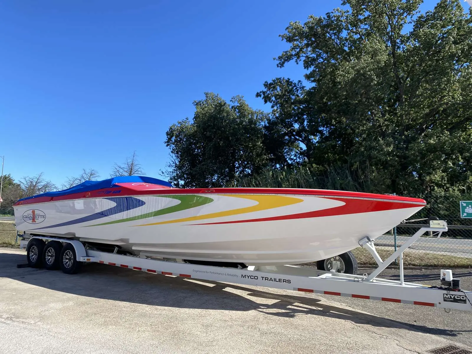 Cigarette Top Gun 38 — Bateau à moteur coloré présenté sur sa remorque dans un espace extérieur.