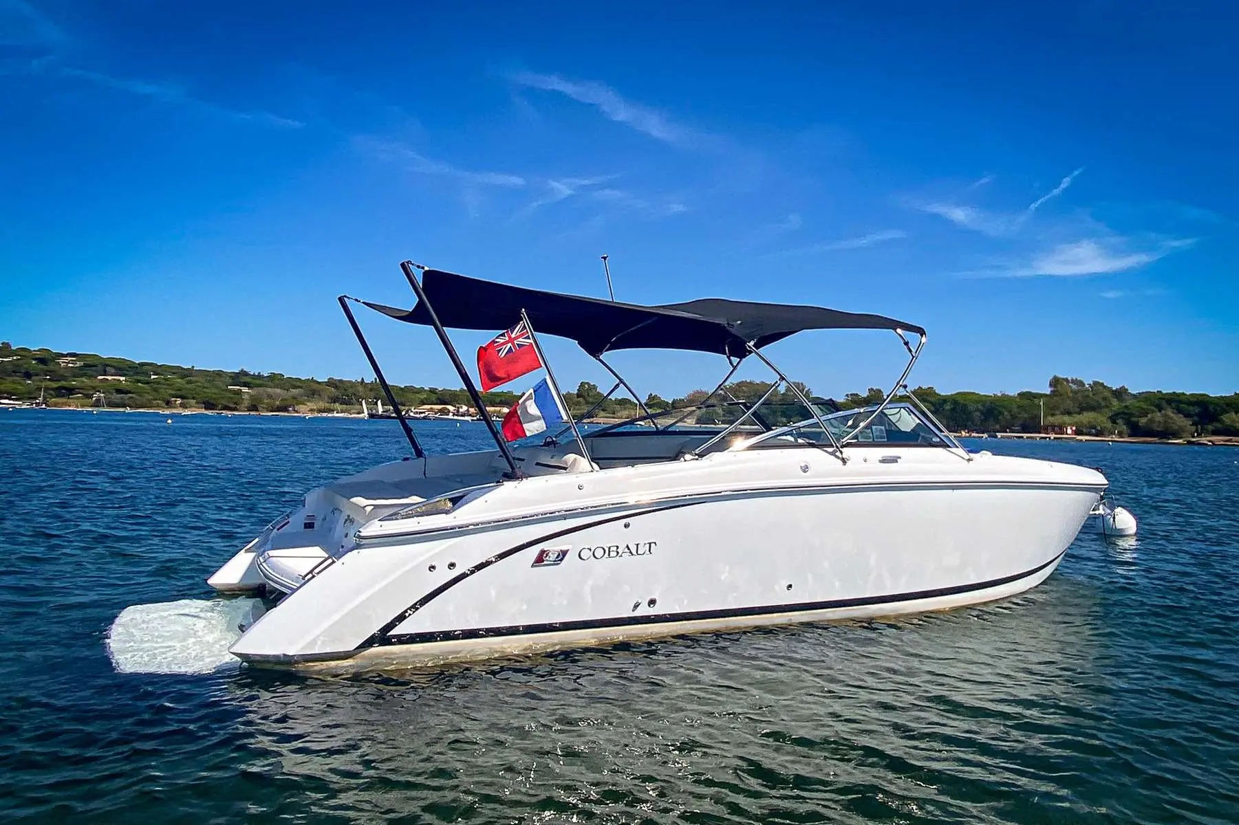 Cobalt R30 — Bateau blanc vu de profil sur l’eau, avec taud et pavillons déployés.