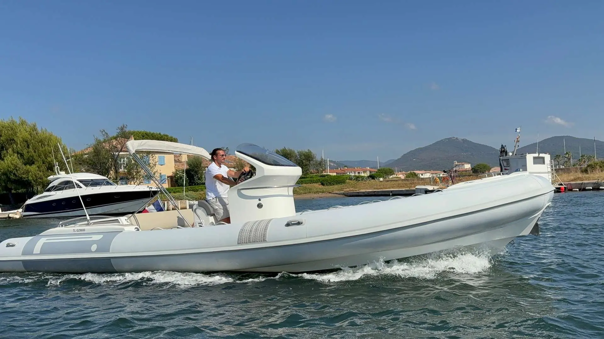 Pirelli Pzero 880 Sport — Bateau semi-rigide blanc naviguant près d'un port, avec un passager à la barre.