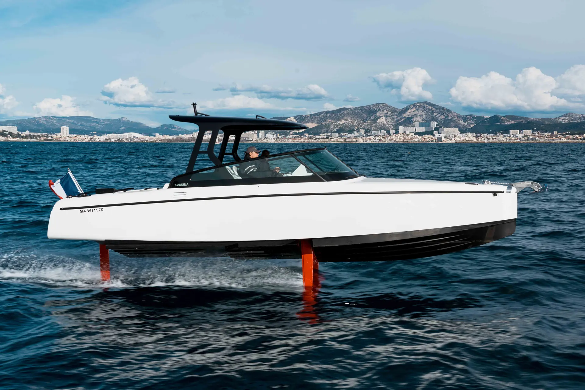 Candela C8 — Bateau à foils blanc vu de profil, en navigation devant une côte montagneuse.