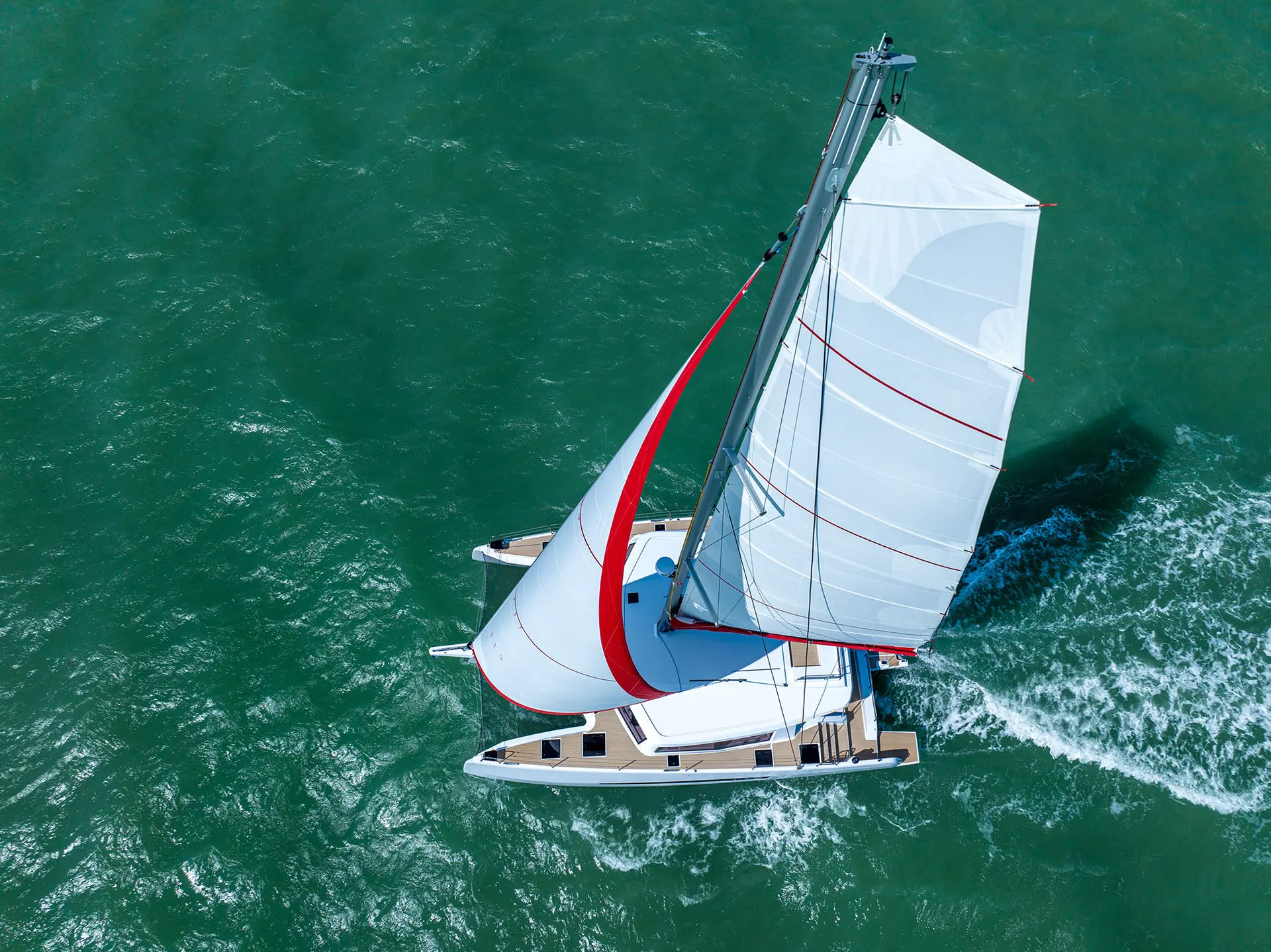 Neel Trimarans Neel 52 — Vue aérienne d’un catamaran à voiles naviguant sur une mer turquoise.