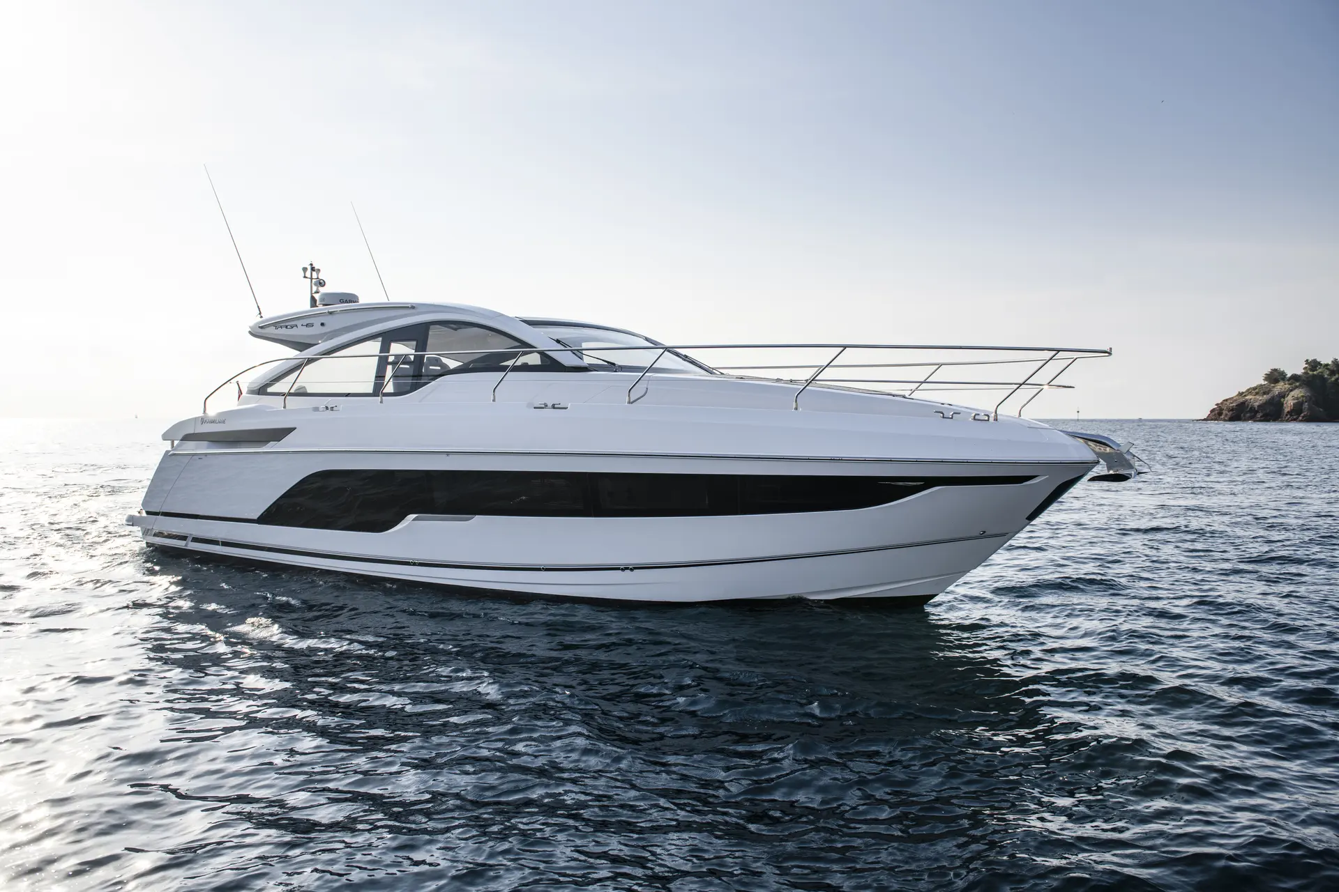 Fairline Targa 45 Open — Bateau à moteur blanc vu de profil sur une mer calme, près d'une côte rocheuse.