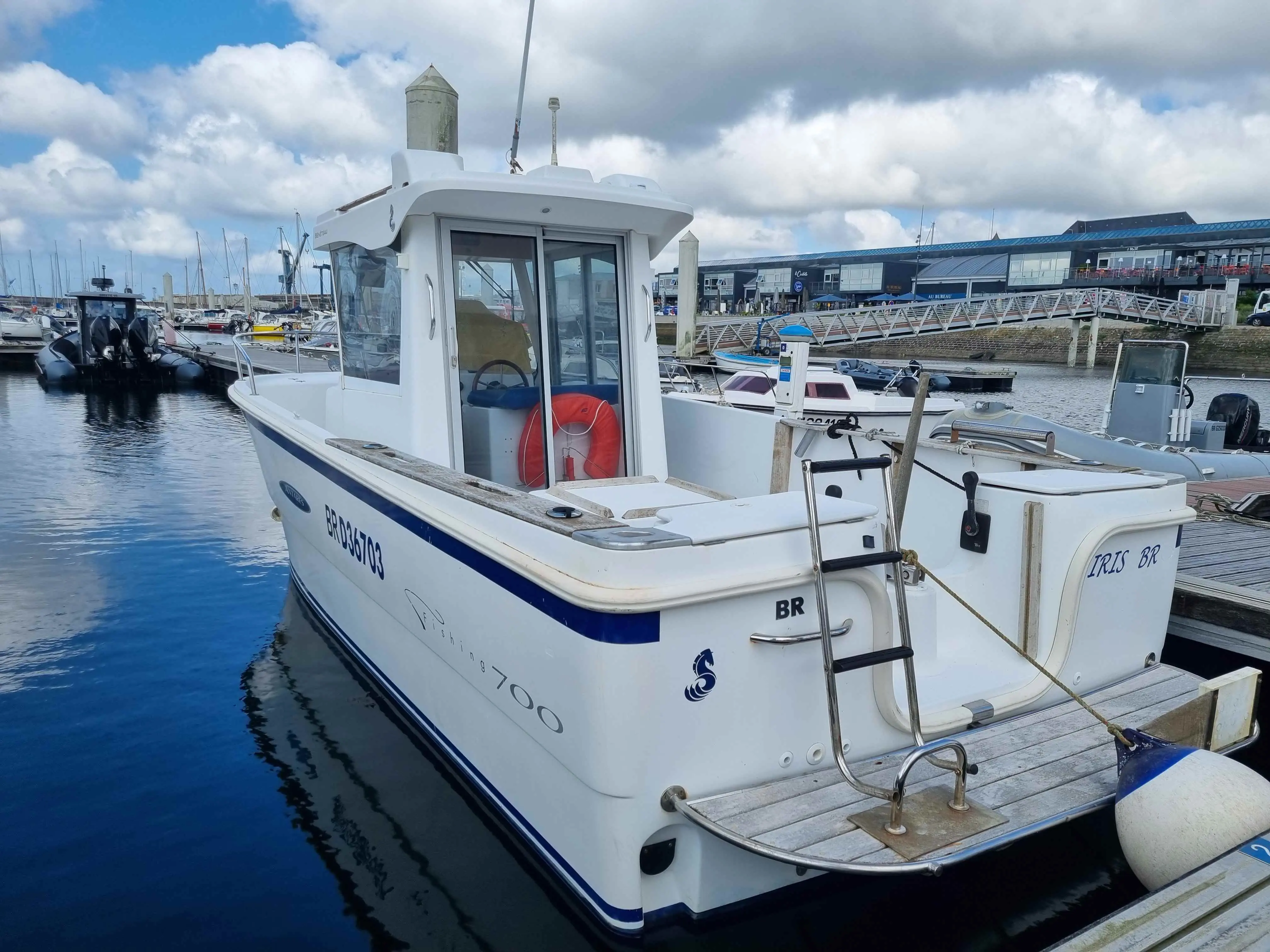 Beneteau Antares 700 Fishing — Bateau à cabine blanche amarré dans un port, vu de trois quarts arrière.