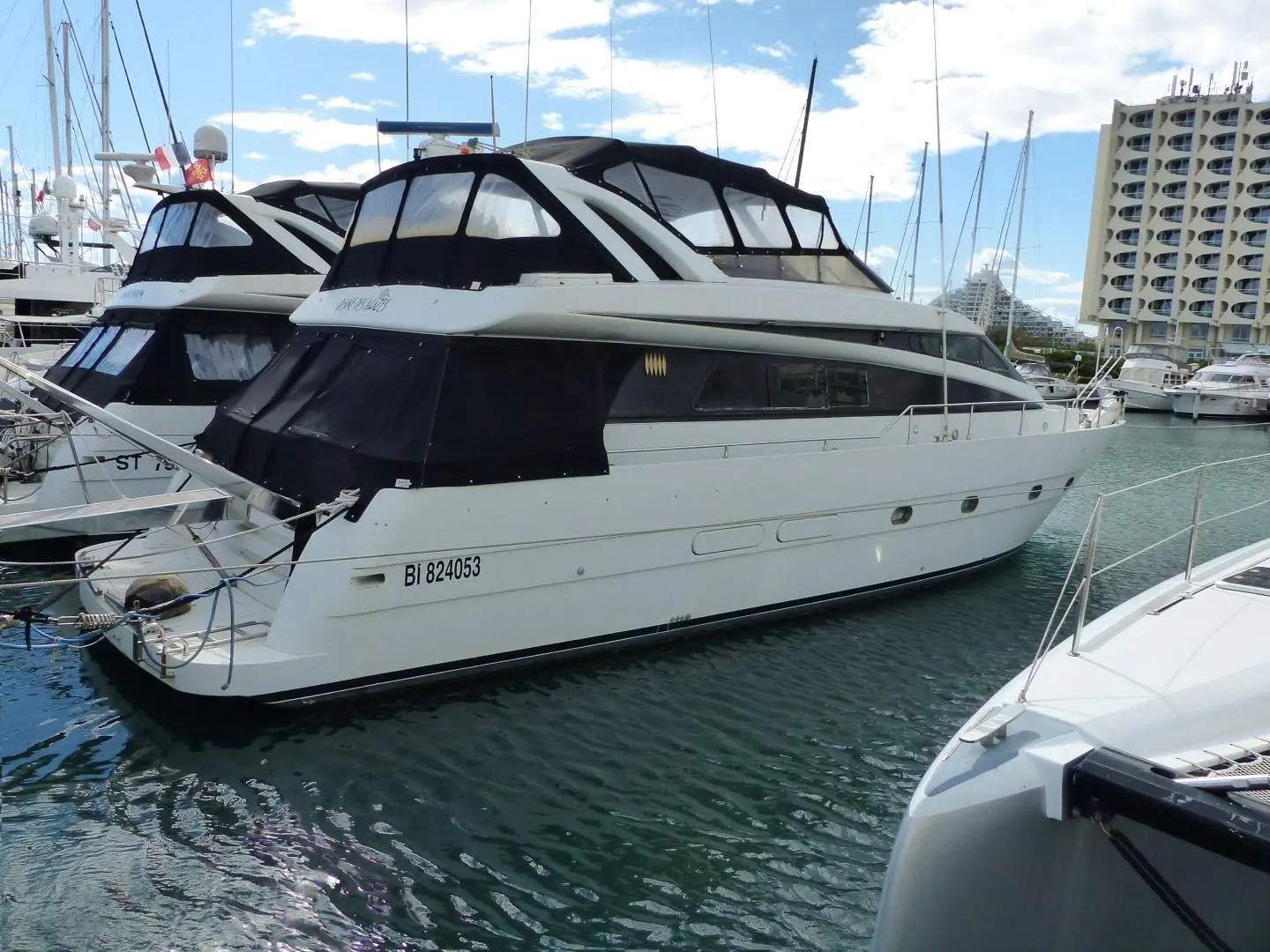 Mondomarine M 60 — Bateau à moteur blanc amarré dans une marina, vu de trois quarts arrière.