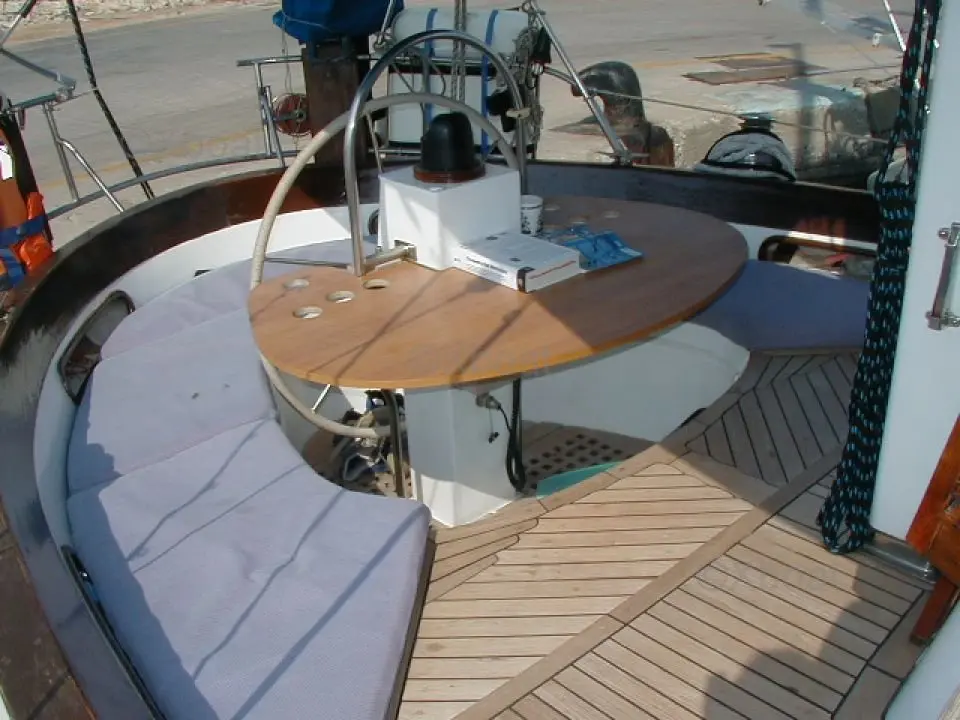 Cheoy Lee 43 — Cockpit arrière avec barre à roue, table en bois et banquettes.