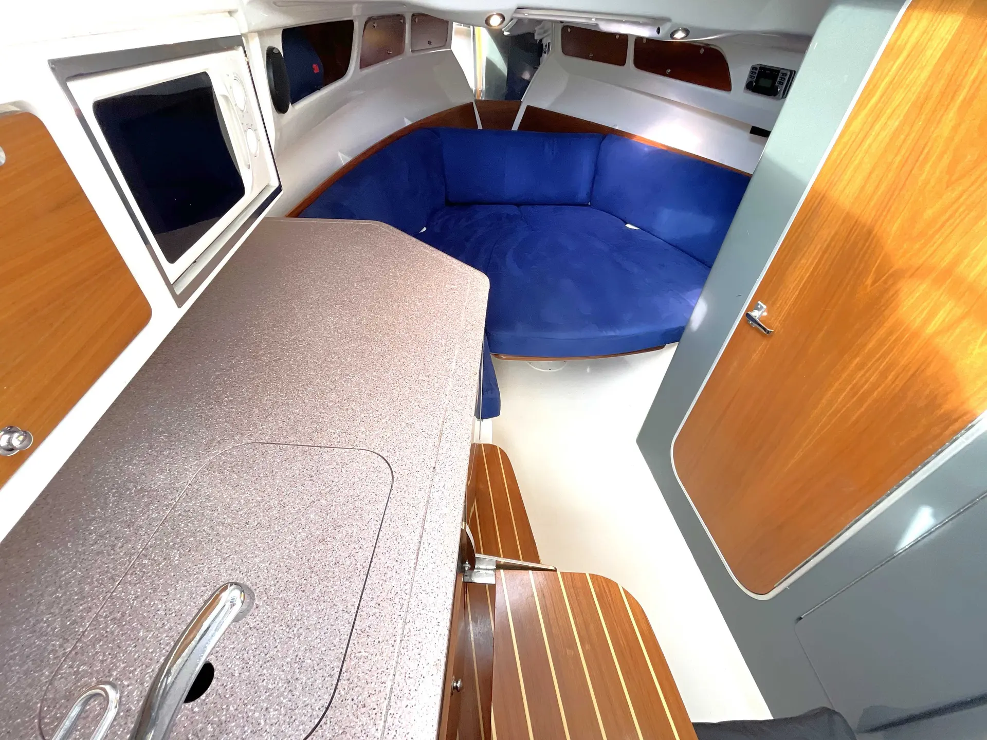 Kelt White Shark 298 — Vue intérieure du carré avec banquette bleue, table et rangements en bois.