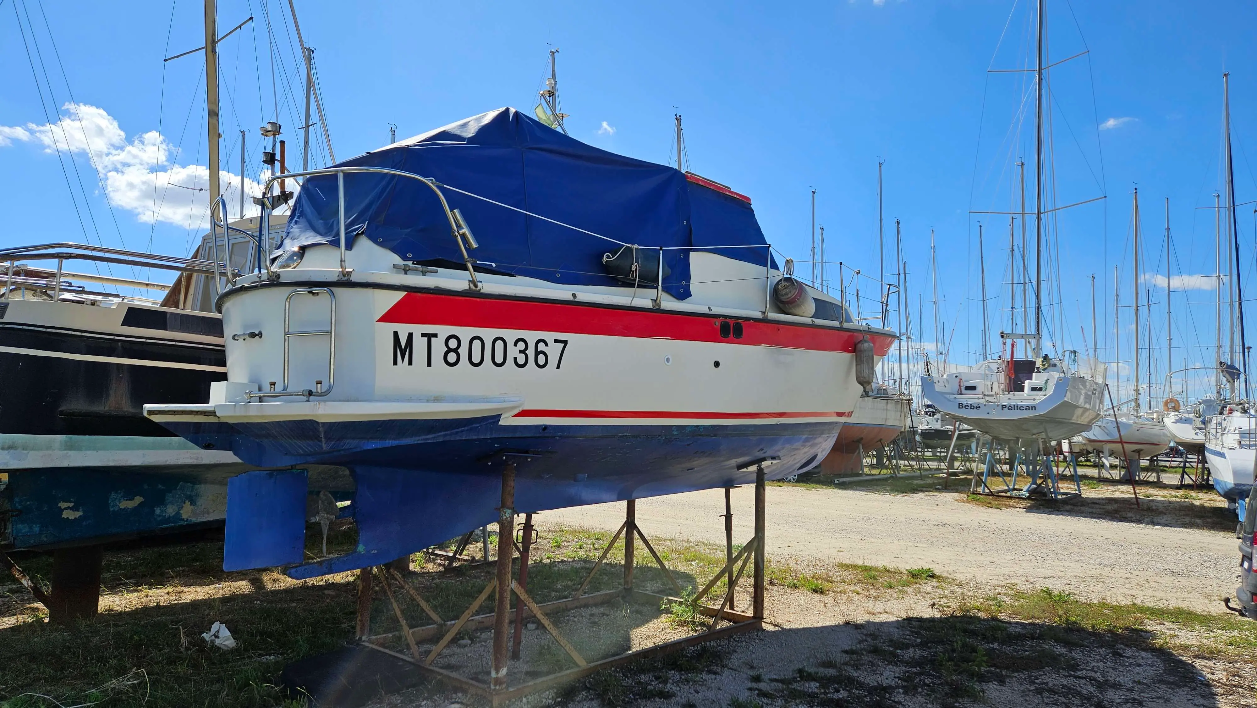 Bonum 25 — Bateau à moteur blanc et rouge présenté sur bers dans un port à sec.