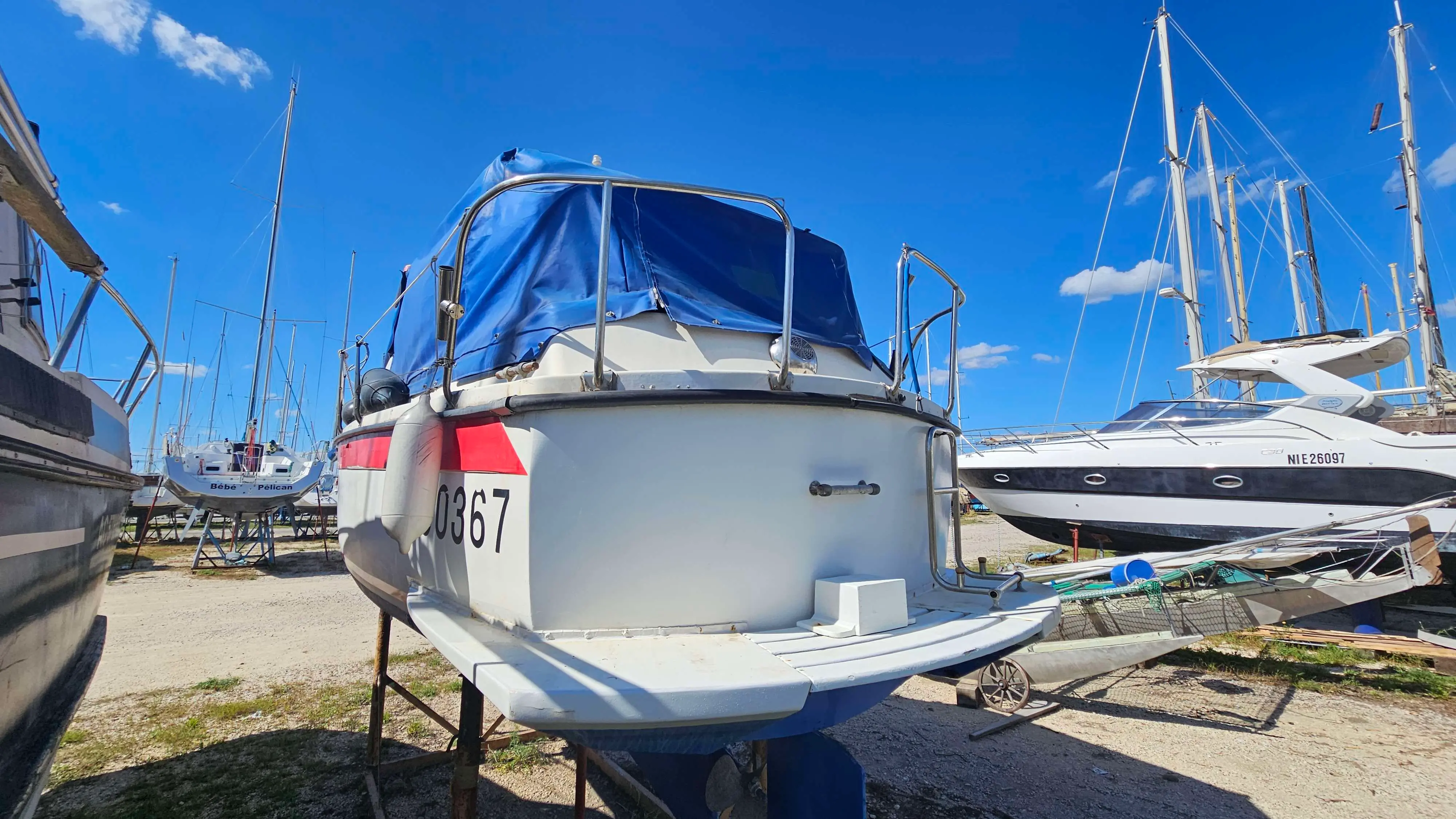 Bonum 25 — Vue arrière d’un bateau blanc à moteur sur bers dans un chantier nautique.