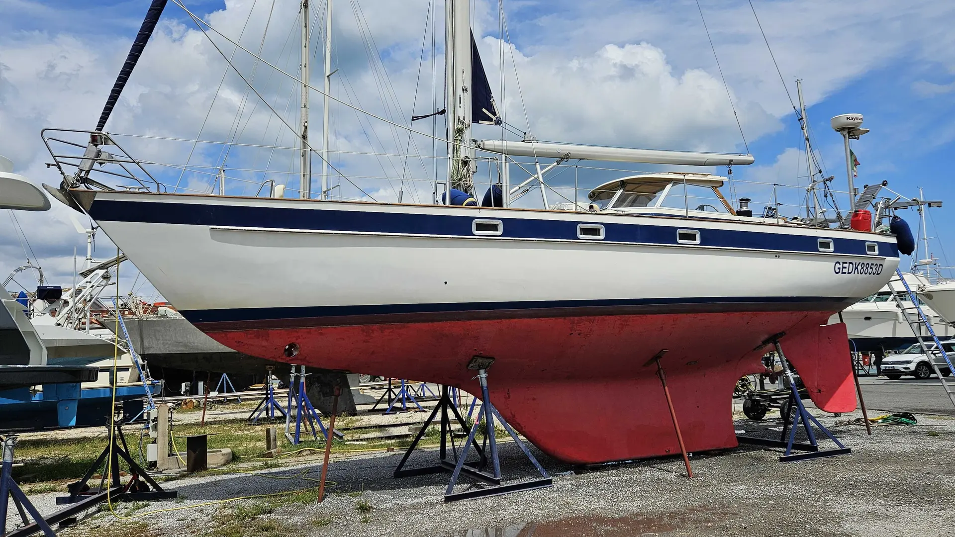 Hallberg Rassy 42 — Voilier vu de profil, à terre sur bers dans une zone de maintenance nautique.