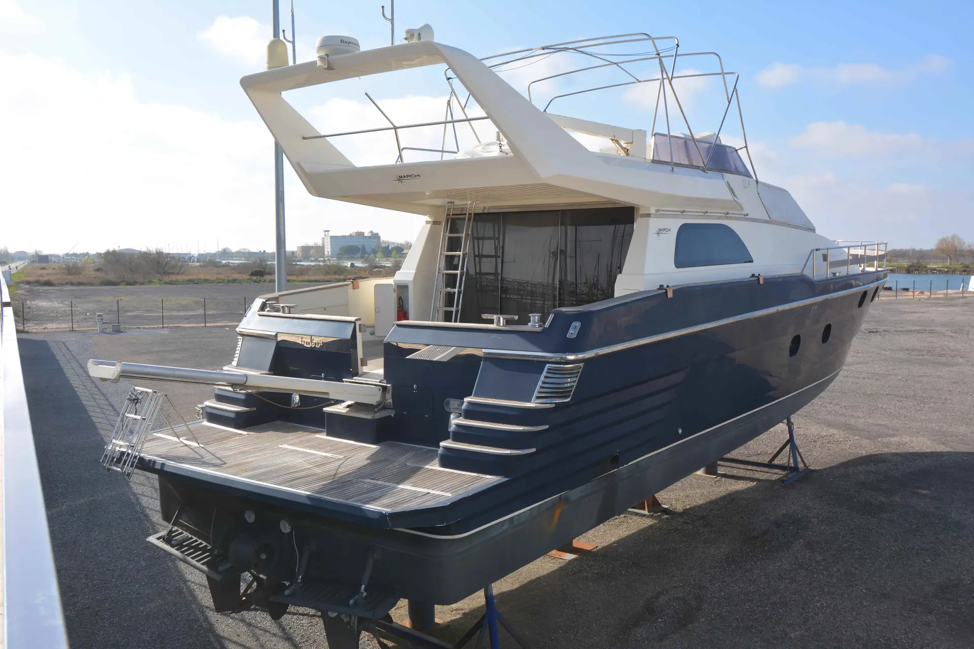 Marchi 65 — Vue arrière trois-quarts d’un bateau à moteur bleu et blanc, à terre.