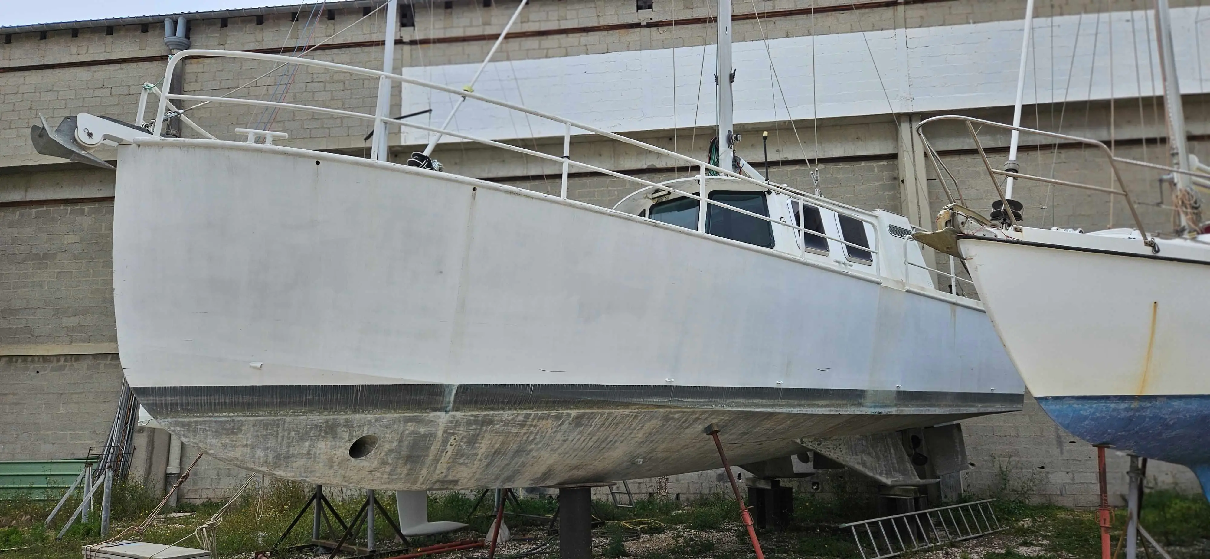 Meta Jnf 39 — Voilier blanc à coque bleue partiellement visible, stationné sur ber dans un chantier naval.