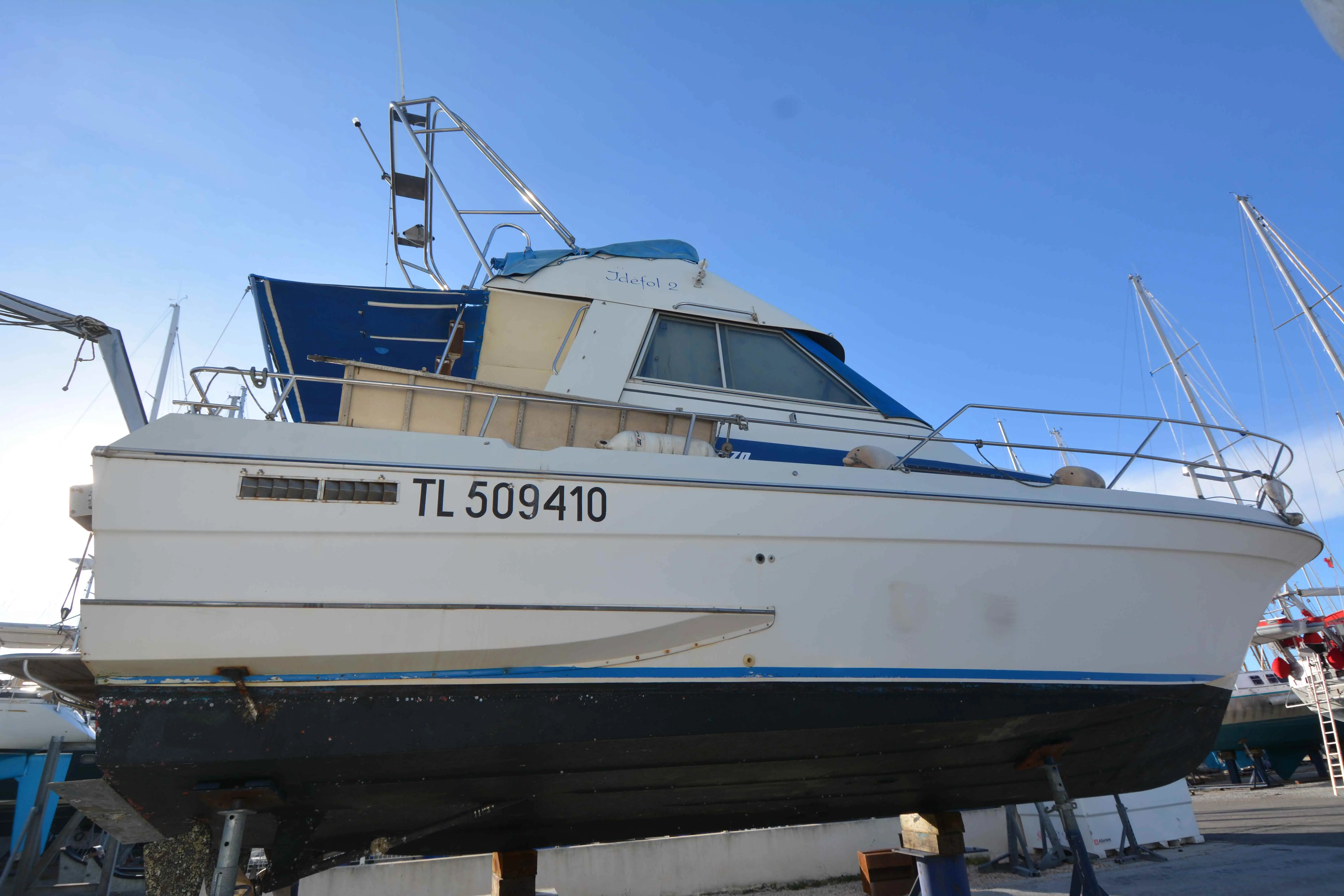 Yachting France Arcoa 970 — Bateau à moteur blanc et bleu photographié à sec dans un chantier naval.