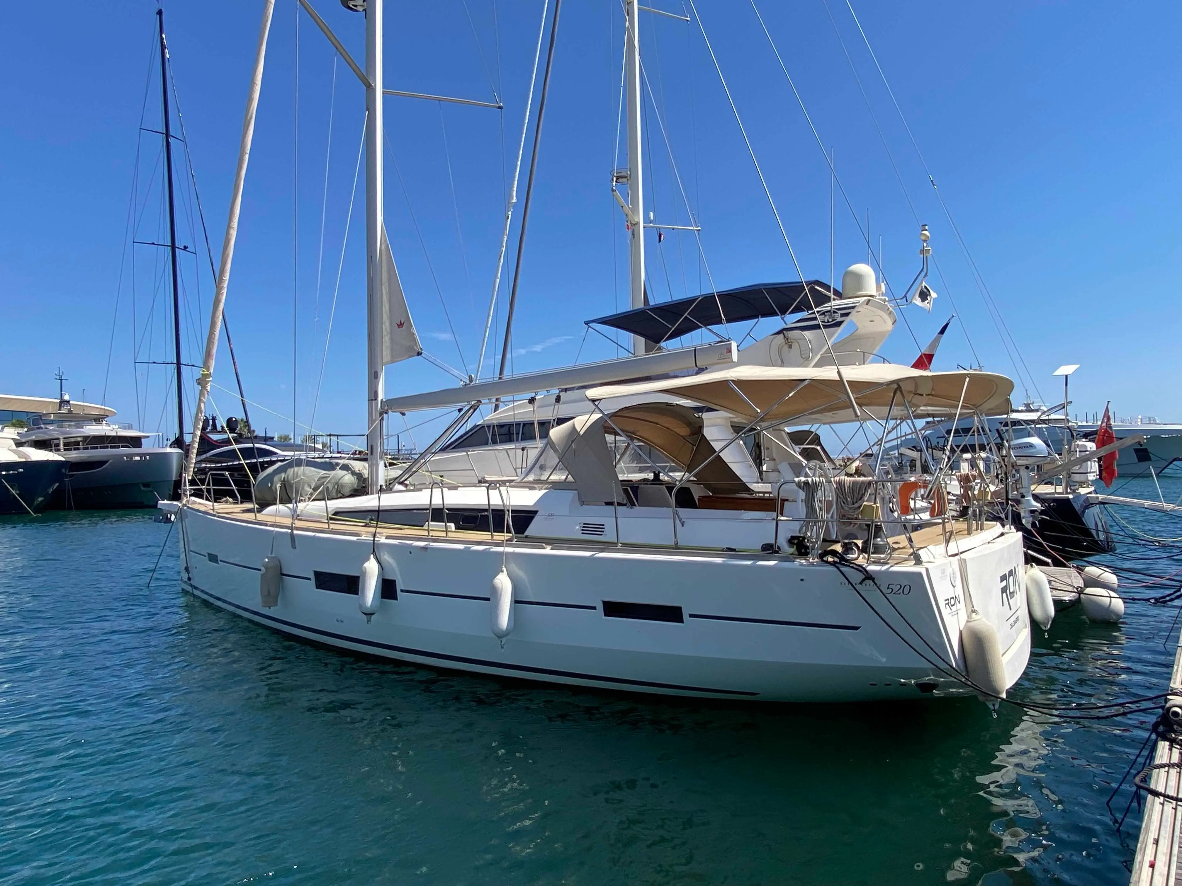 Dufour 520 Grand Large — Voilier blanc vu de trois-quarts arrière dans une marina ensoleillée.
