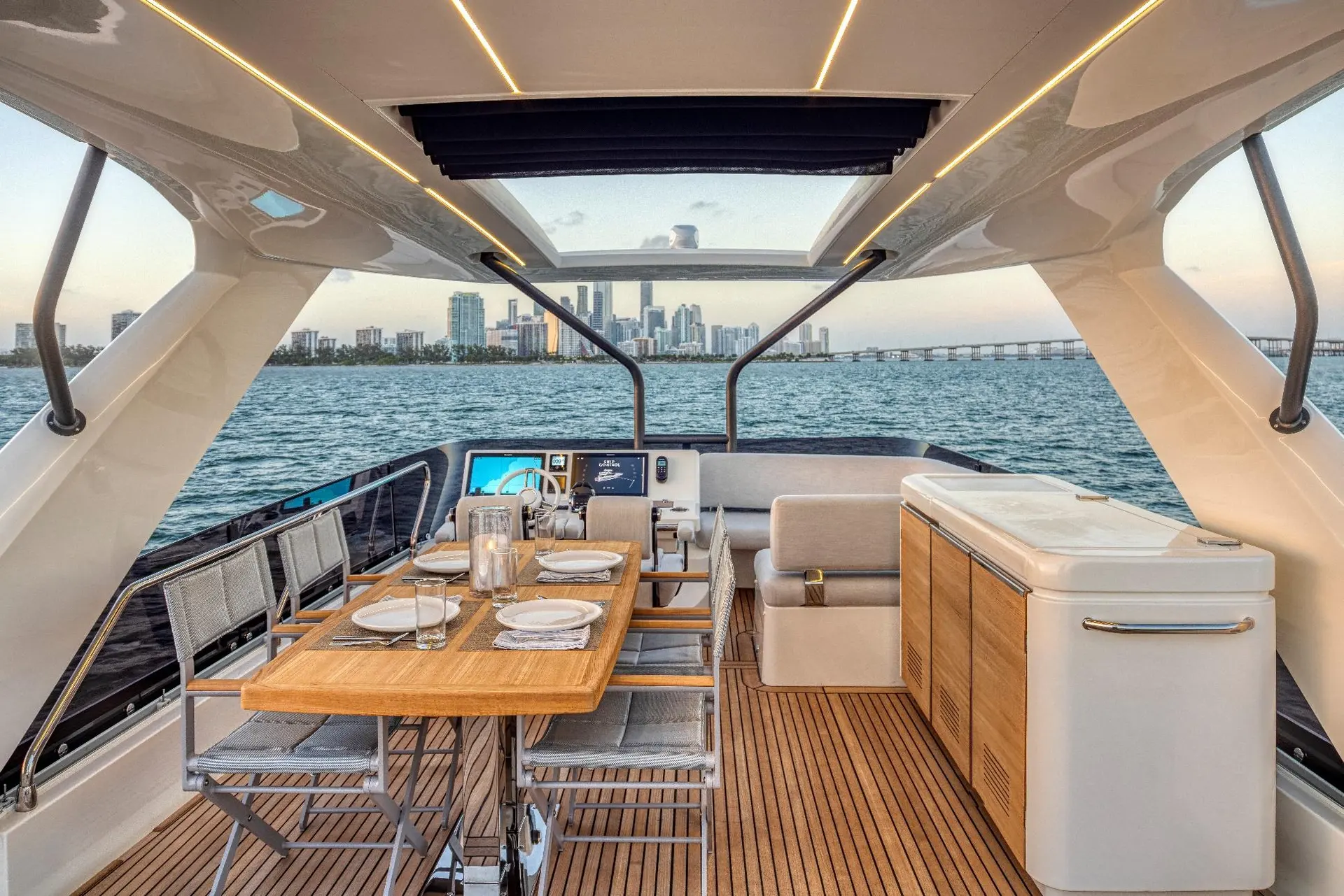 Prestige Yachts 690 — Cockpit arrière aménagé avec table à manger, cuisine extérieure et vue sur la ville.