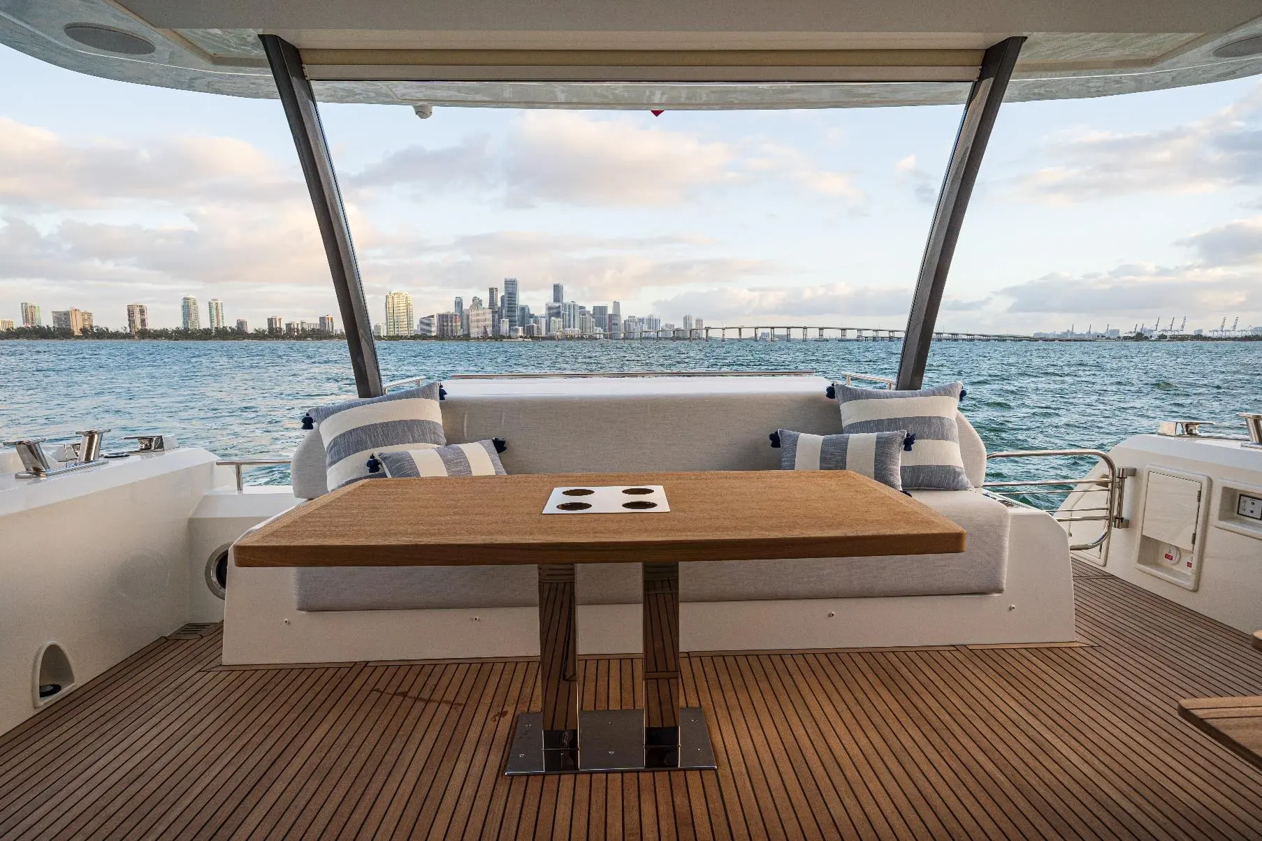 Prestige Yachts 690 — Cockpit arrière avec table et banquette face à une skyline côtière.
