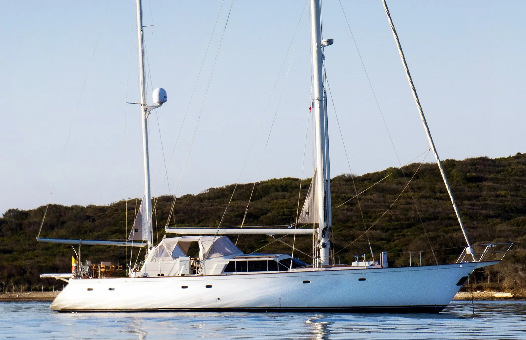 Vaton 70 — Voilier blanc photographié de profil sur une eau calme, devant une côte boisée.