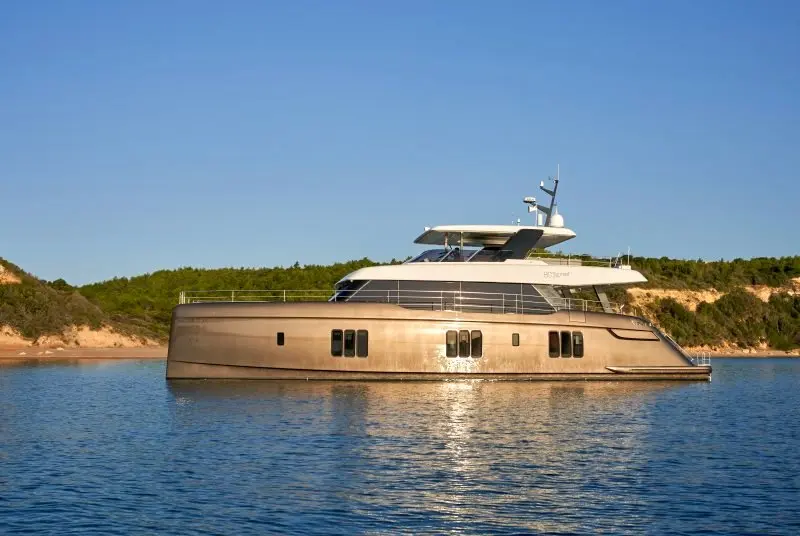 Sunreef Yachts Sunreef 80 — Vue de profil d’un yacht à moteur amarré devant une côte boisée.
