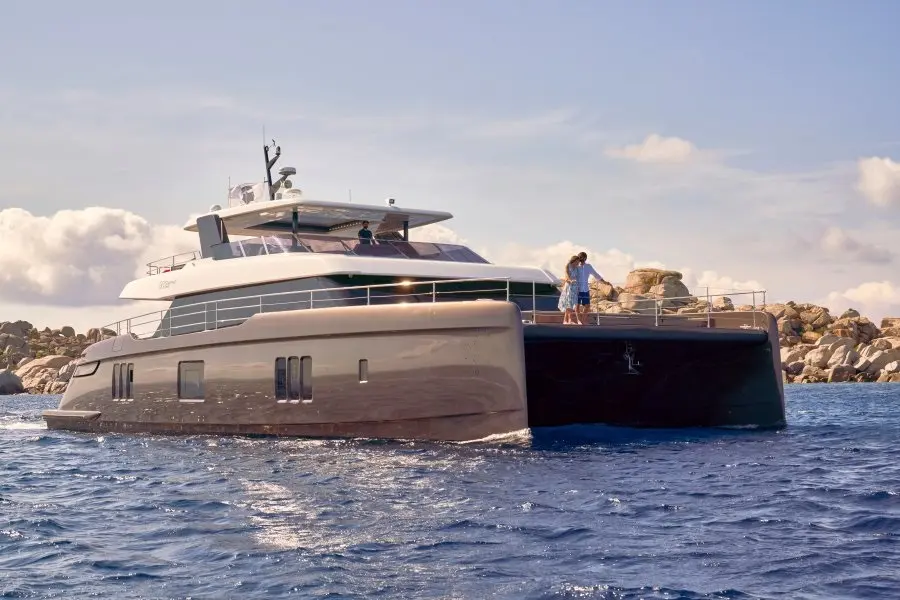 Sunreef Yachts Sunreef 80 — Catamaran à moteur blanc naviguant près d'une digue rocheuse.