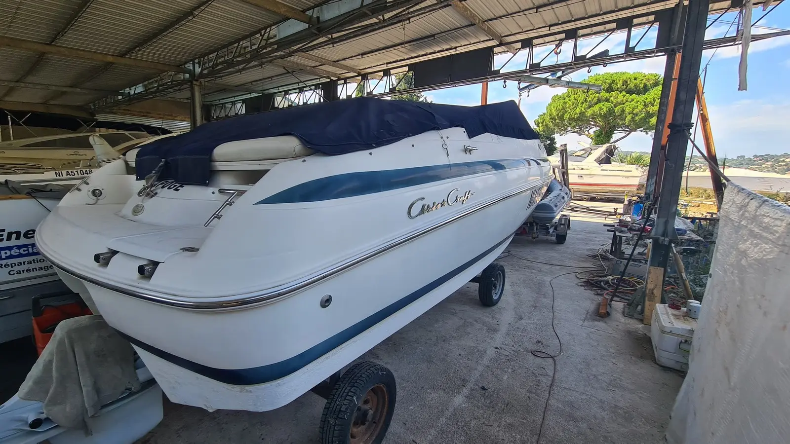 Chris Craft 210 — Bateau blanc à liserés bleus photographié sur remorque dans un hangar.