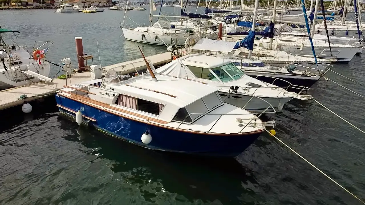 Coronet 27 Sea Farer — Vedette à cabine blanche et coque bleue amarrée dans un port de plaisance.