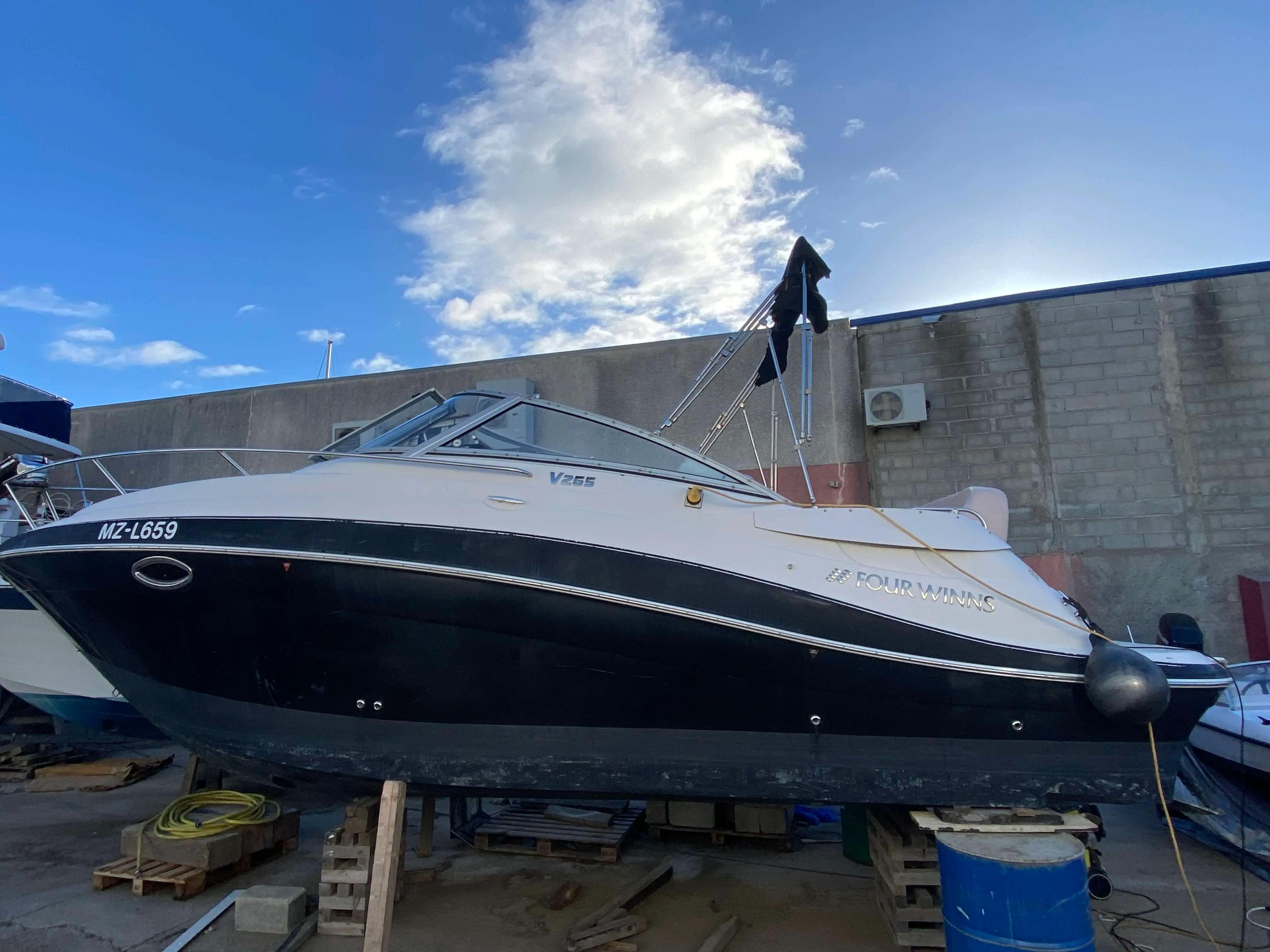Four Winns V 265 — Vue latérale d’un bateau à moteur blanc et noir présenté à terre.