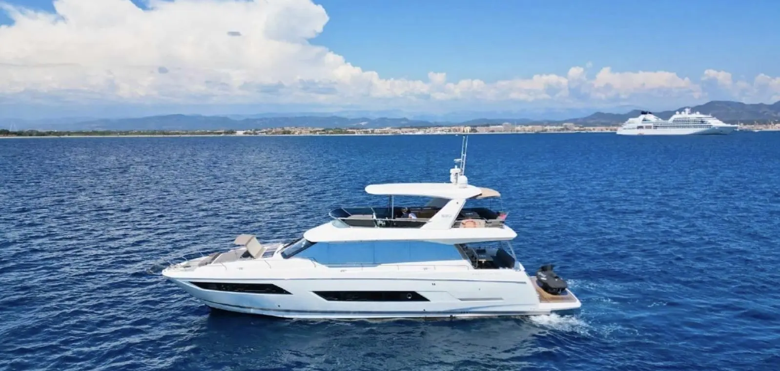 Jeanneau Prestige 680 — Bateau à moteur blanc vu de profil sur une mer bleue, avec une côte en arrière-plan.