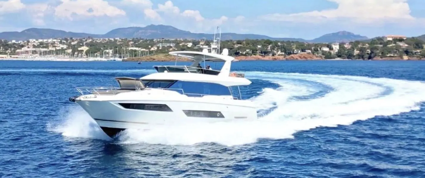 Jeanneau Prestige 680 — Bateau à moteur blanc naviguant à vive allure devant une côte méditerranéenne.