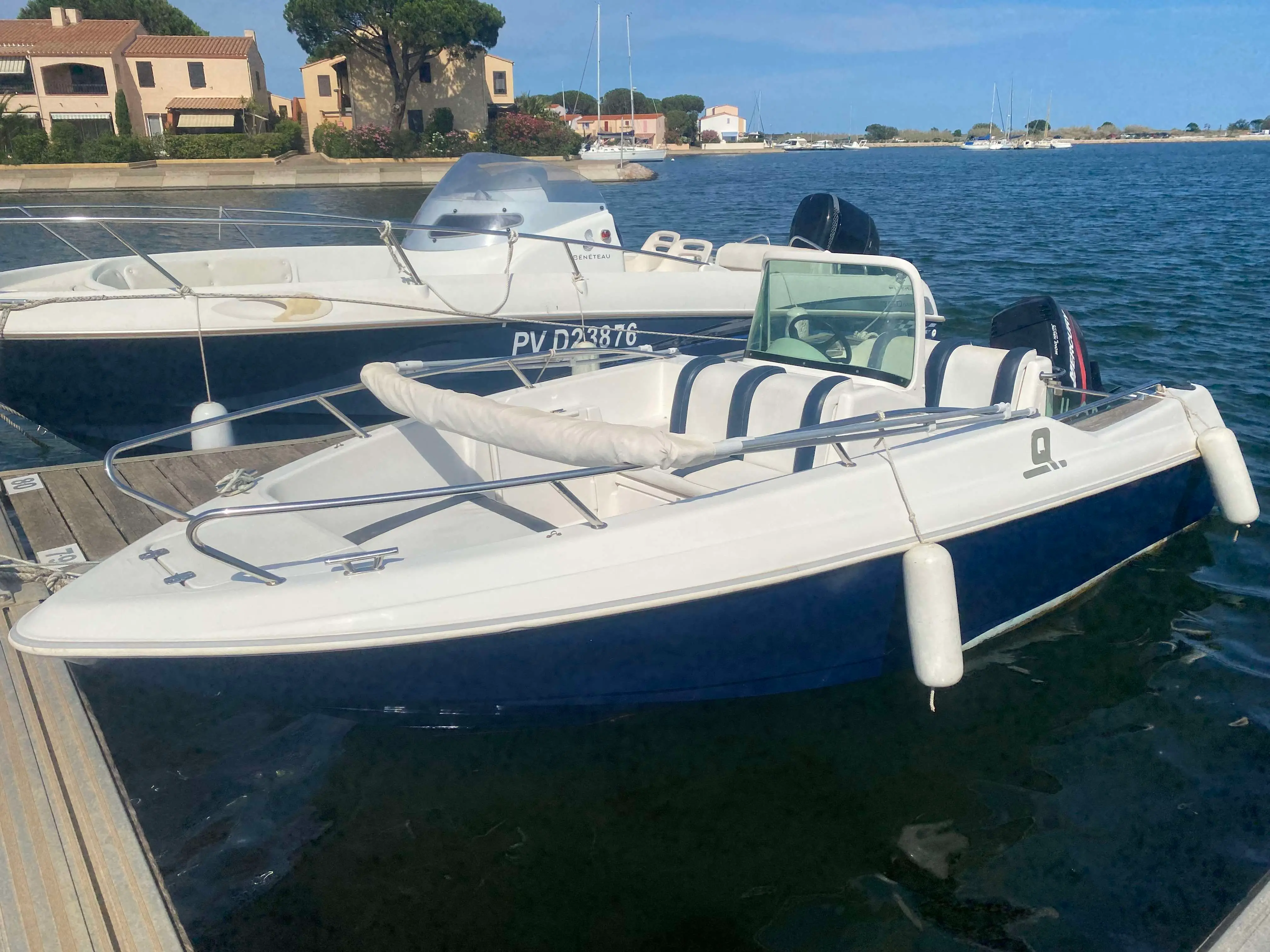 Quicksilver 500 Commander — Bateau à moteur blanc et bleu amarré dans un port, vu de trois quarts.