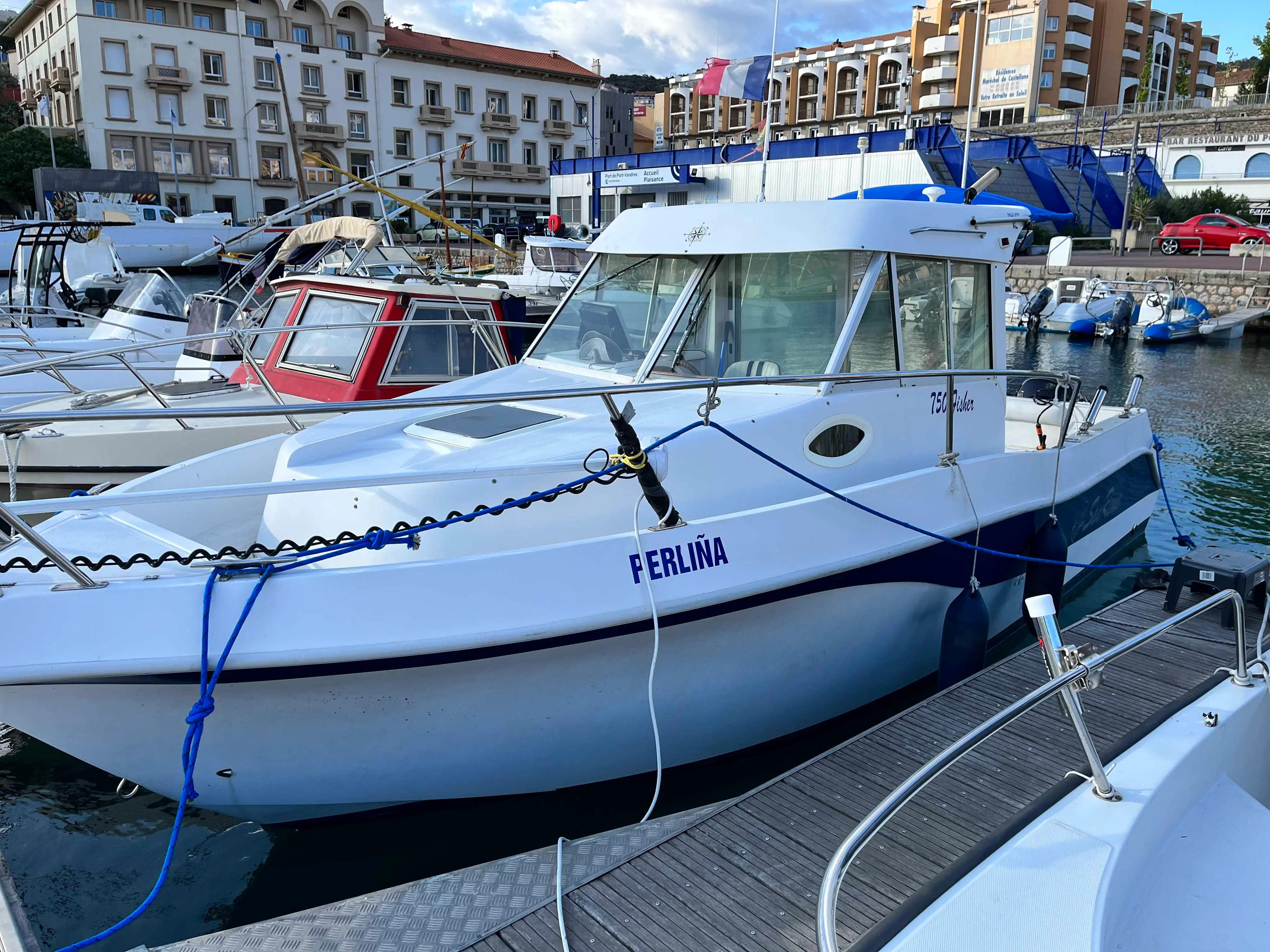 San Remo 750 Fisher — Bateau à cabine blanche et bleue amarré dans un port urbain.