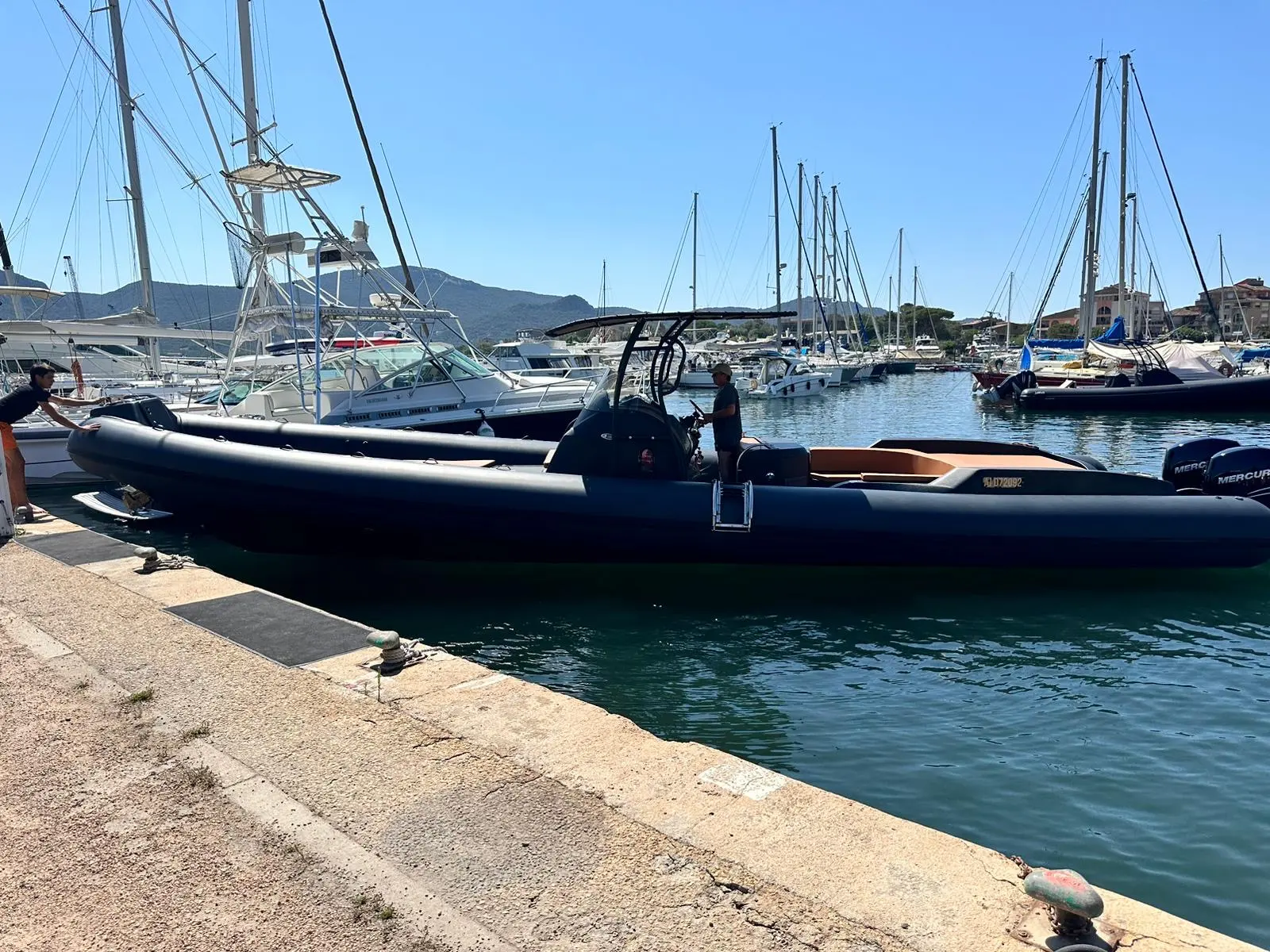 Sacs Stratos 12 — Bateau pneumatique noir amarré dans un port, avec plusieurs voiliers en arrière-plan.