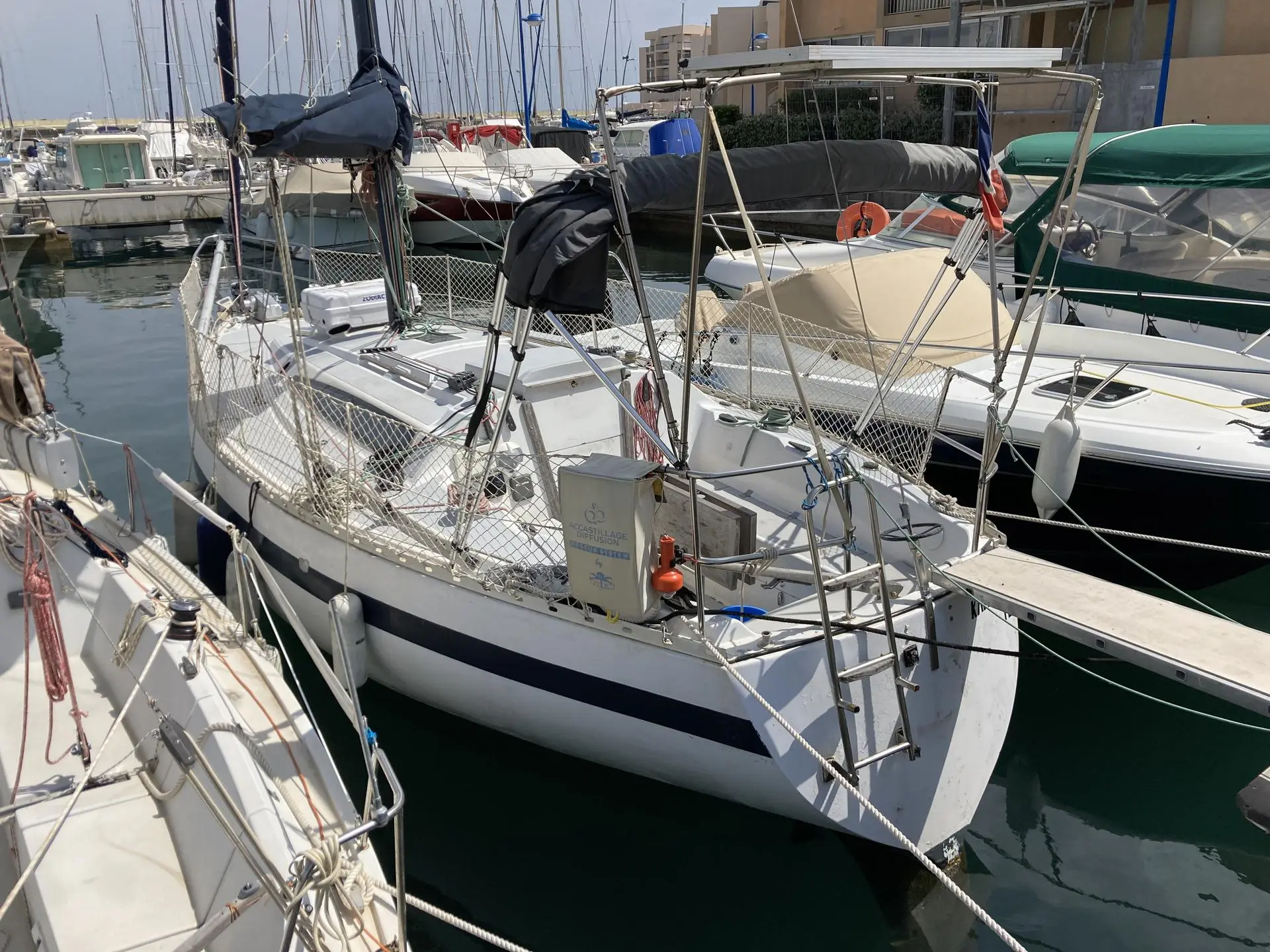 Neptune Smap Trident 80 — Voilier blanc à bande bleue amarré dans un port de plaisance.