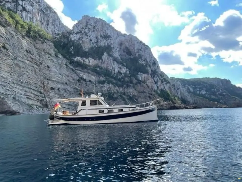 Copino 53 — Bateau à moteur vu de profil, ancré devant des falaises, par temps ensoleillé.