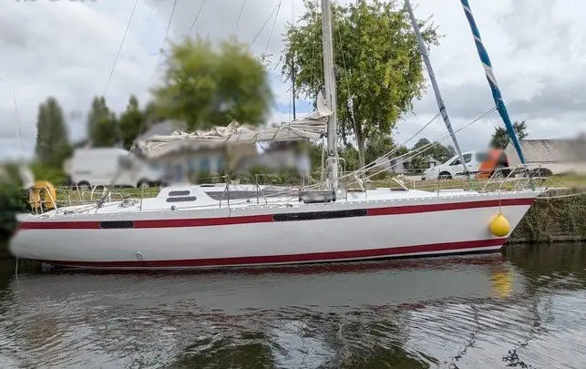 Pouvreau Rivage 39 — Voilier blanc à bande rouge amarré le long d'une berge.