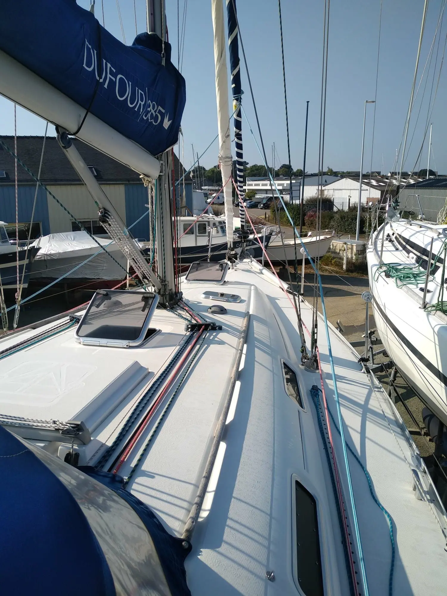 Dufour 385 — Vue du pont avant d’un voilier amarré, avec gréement et capote de grand-voile.