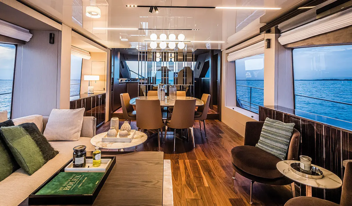Cranchi Sessantasette 67 — Salon intérieur avec espace repas, sièges et larges baies donnant sur la mer.