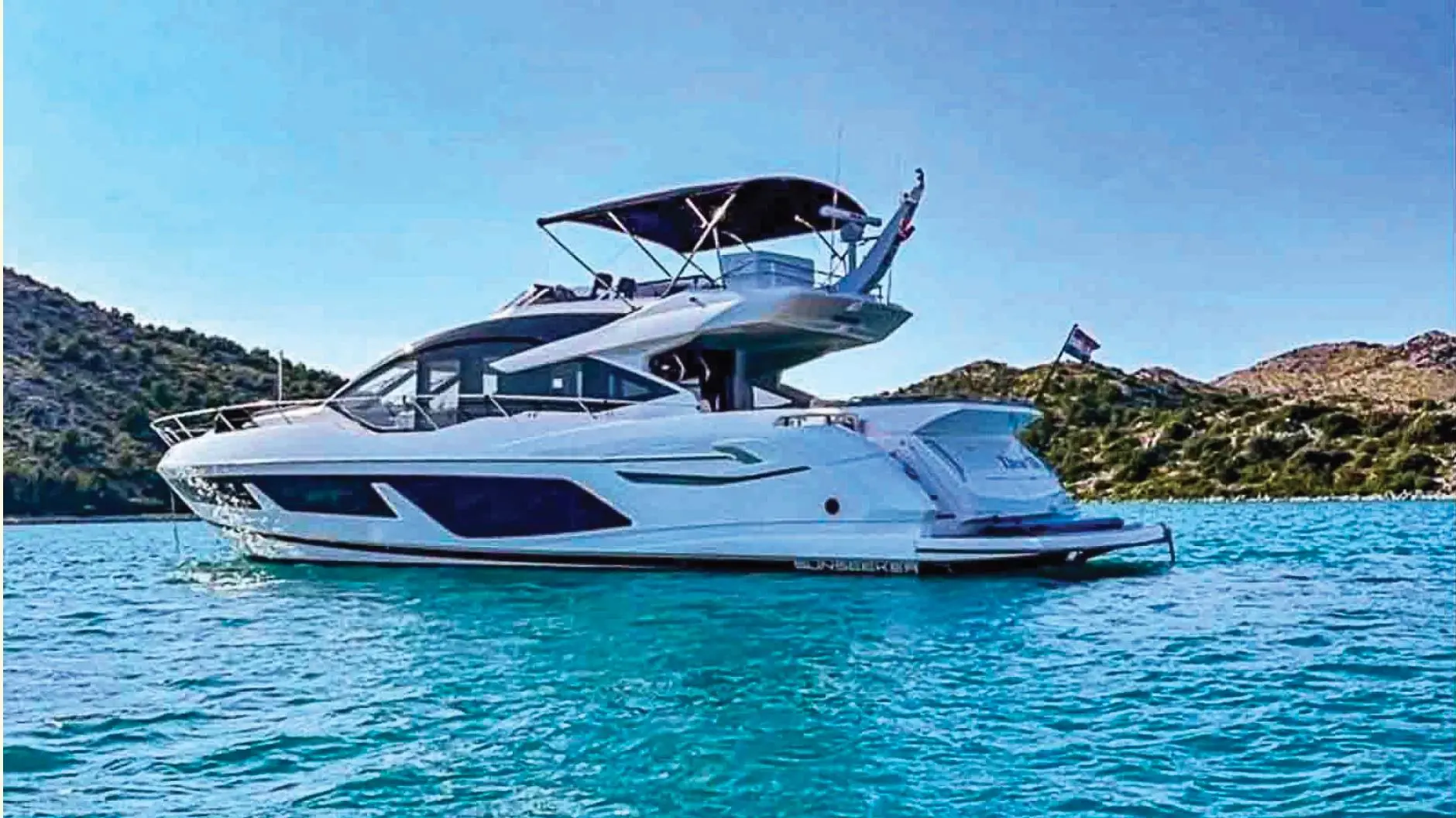 Sunseeker Sport Yacht 74 — Bateau à moteur blanc photographié de profil sur une eau turquoise.