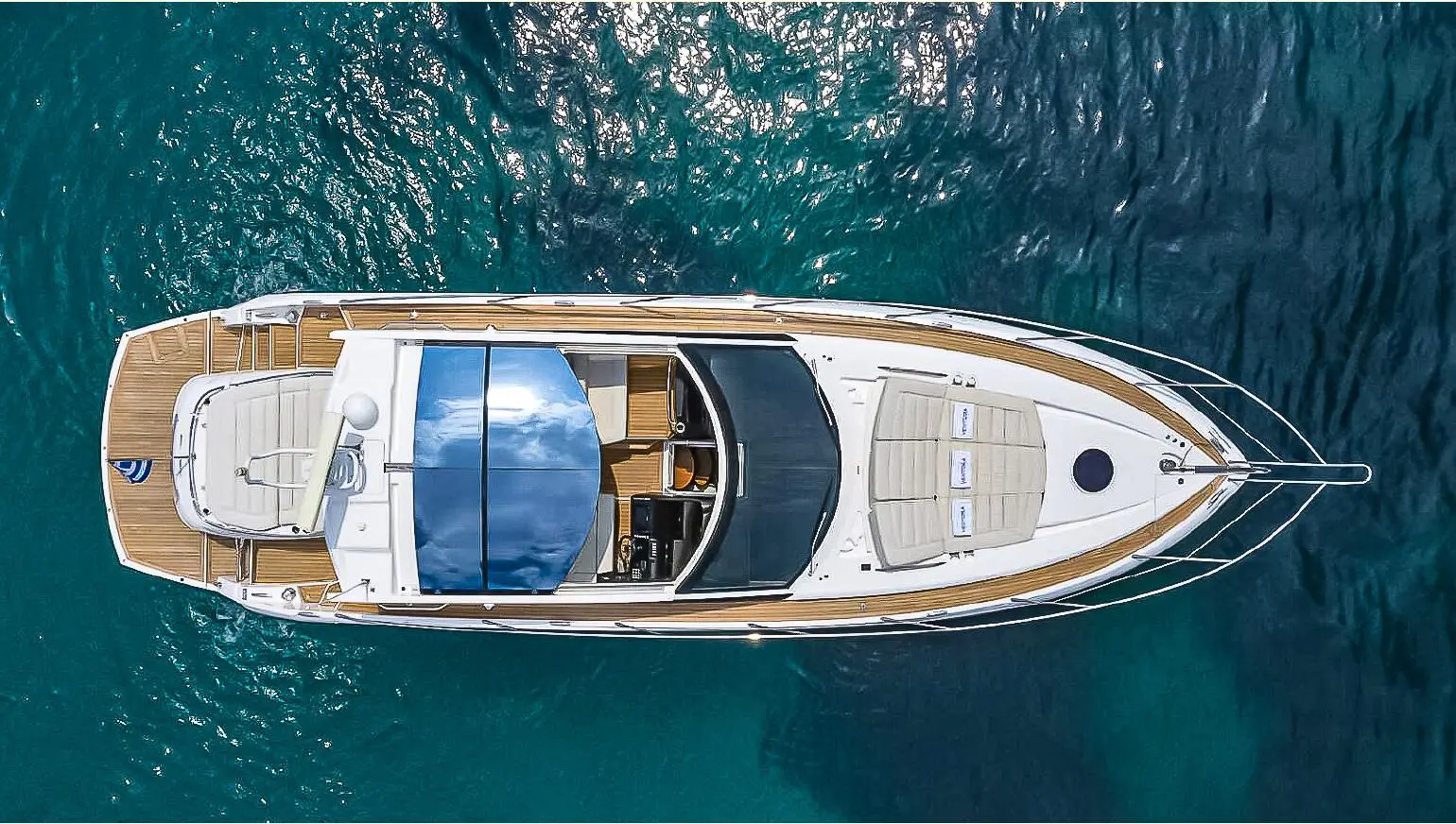 Sunseeker San Remo — Vue aérienne d’un bateau blanc avec pont en teck, amarré sur une mer turquoise.