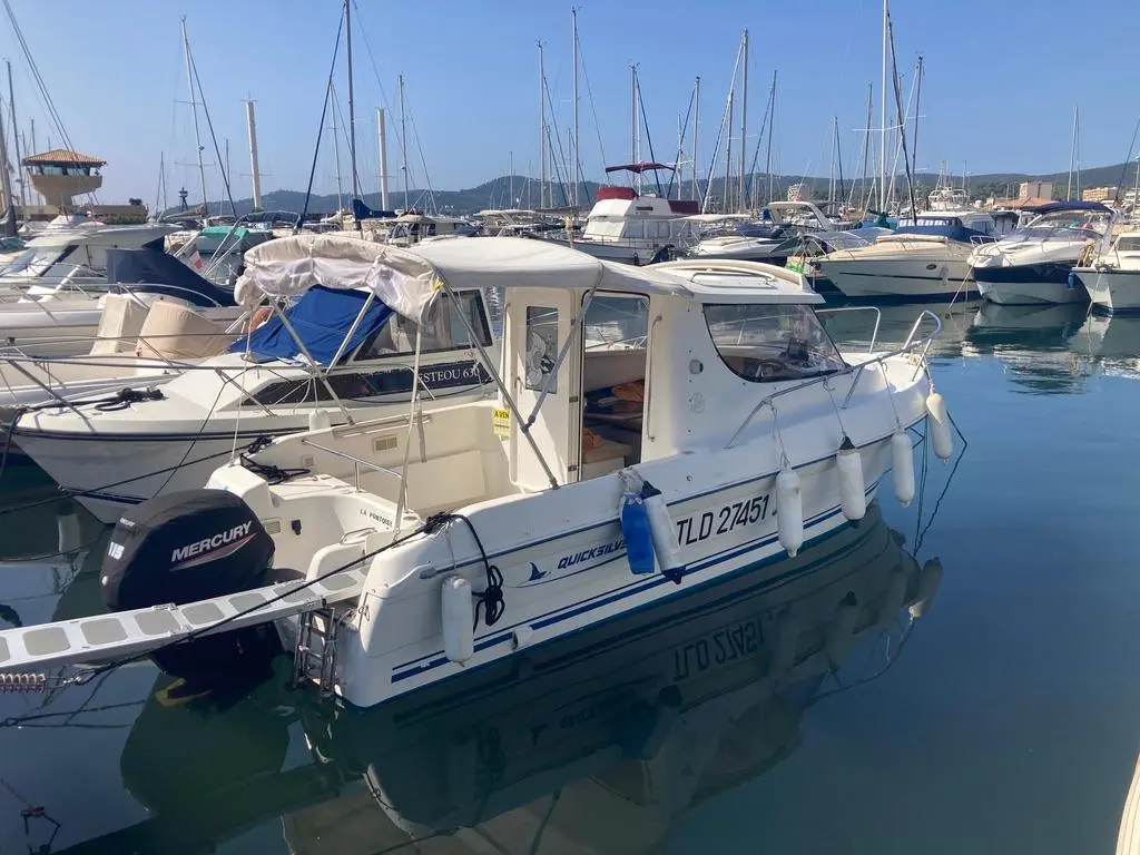Quicksilver 650 Week-End — Bateau à moteur blanc amarré dans un port, vu de trois quarts arrière.