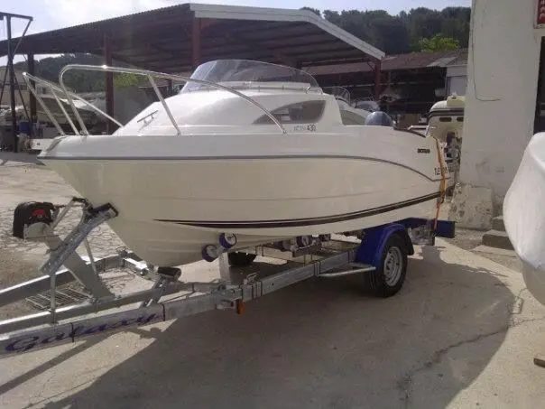 Quicksilver Activ 430 Cabin — Bateau à moteur blanc sur remorque, photographié de trois quarts dans une cour.