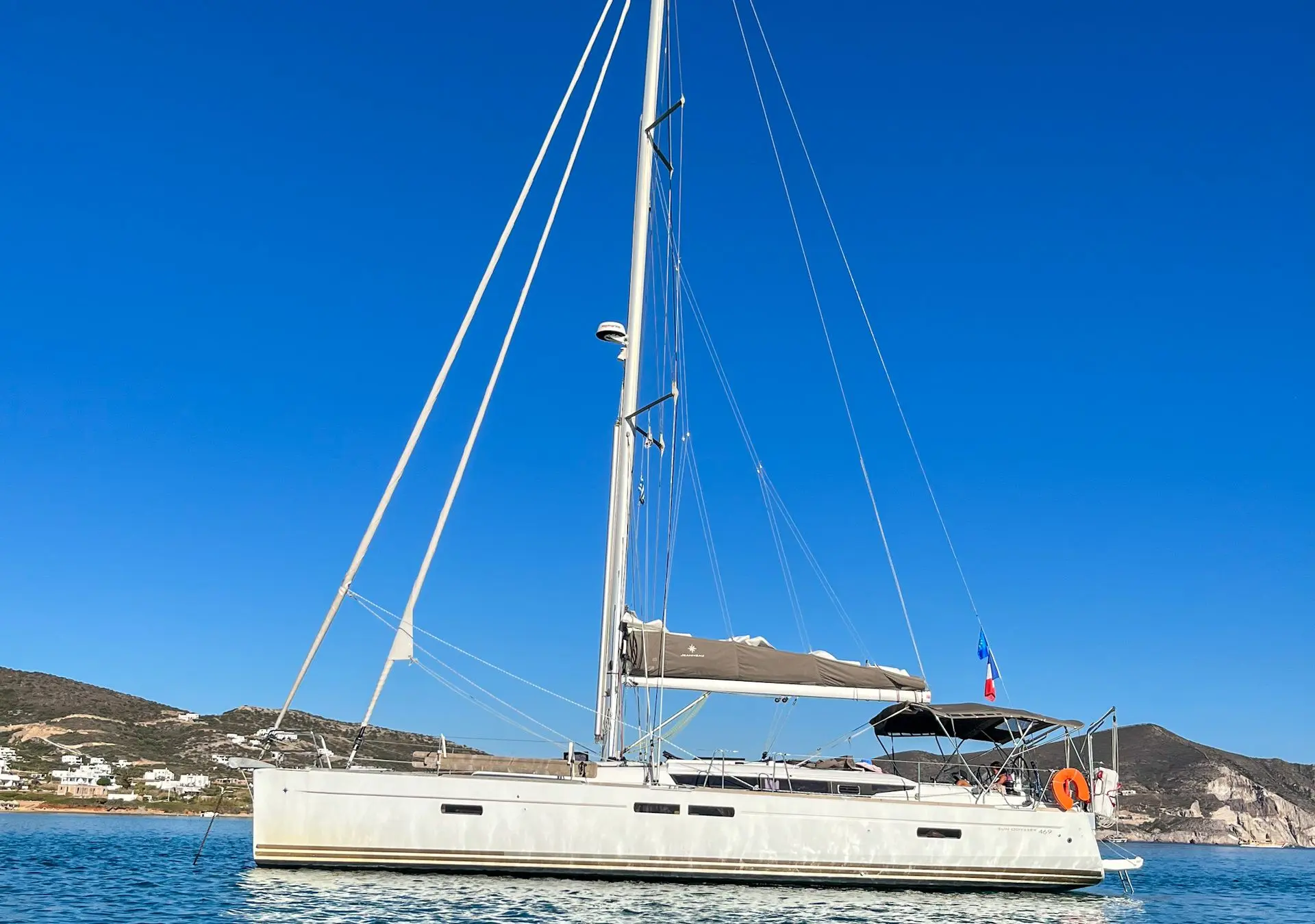 Jeanneau Sun Odyssey 469 — Voilier blanc vu de profil au mouillage, avec mât, bimini et pavillon français.