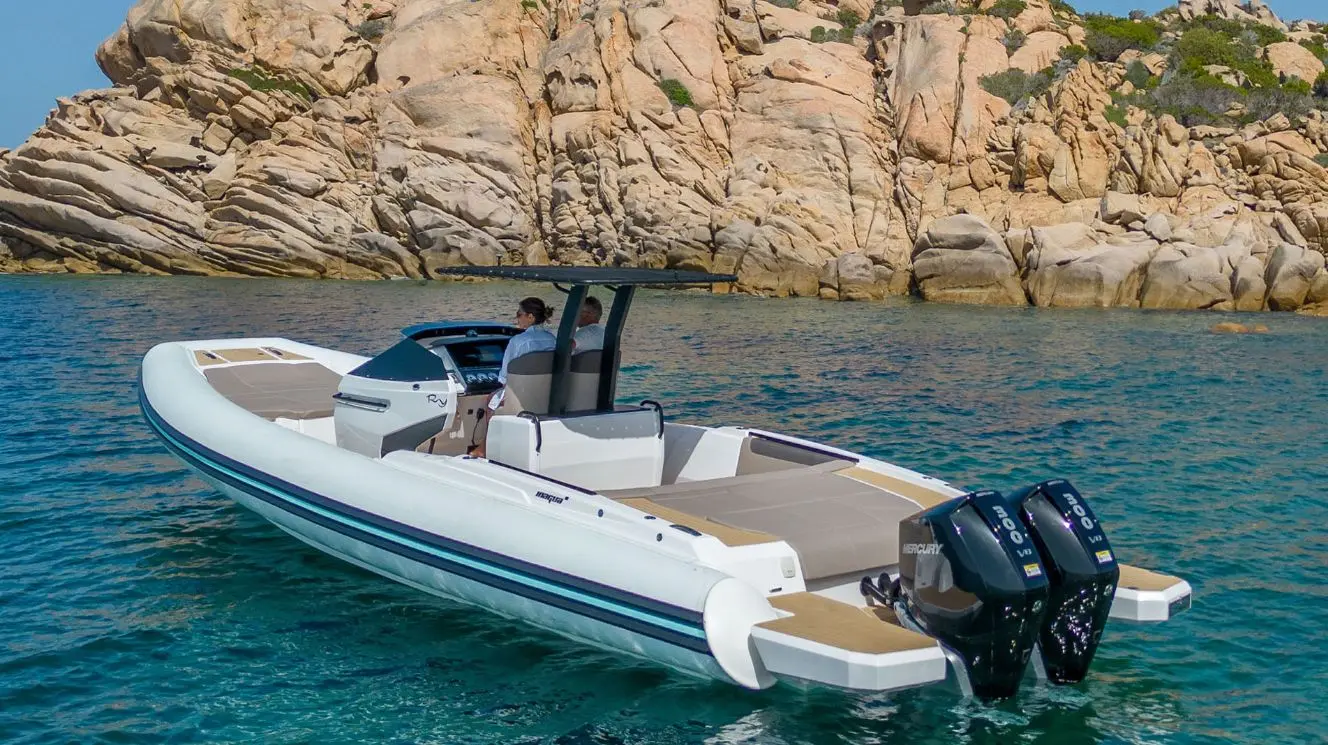 Rio Yachts Inagua — Bateau semi-rigide blanc équipé de deux moteurs hors-bord, au mouillage devant des rochers.