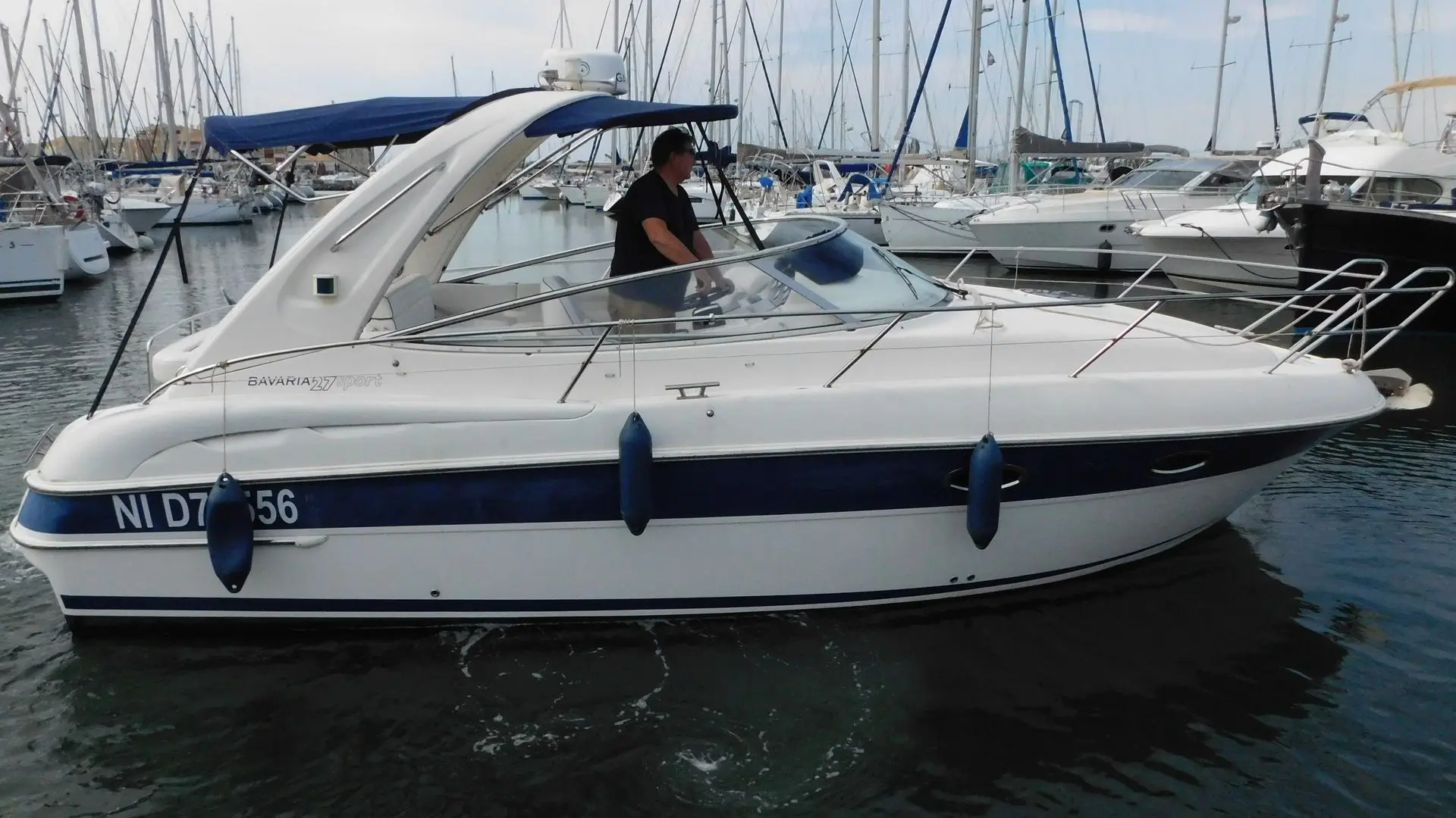 Bavaria 27 Sport — Bateau à moteur blanc et bleu amarré dans une marina, vu de profil.