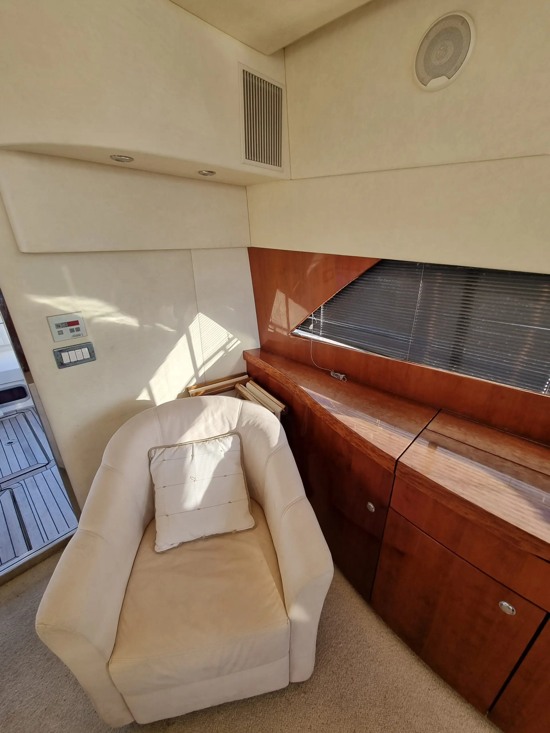 Fairline Phantom 50 — Vue partielle d’un salon intérieur avec fauteuil, rangements en bois et stores.