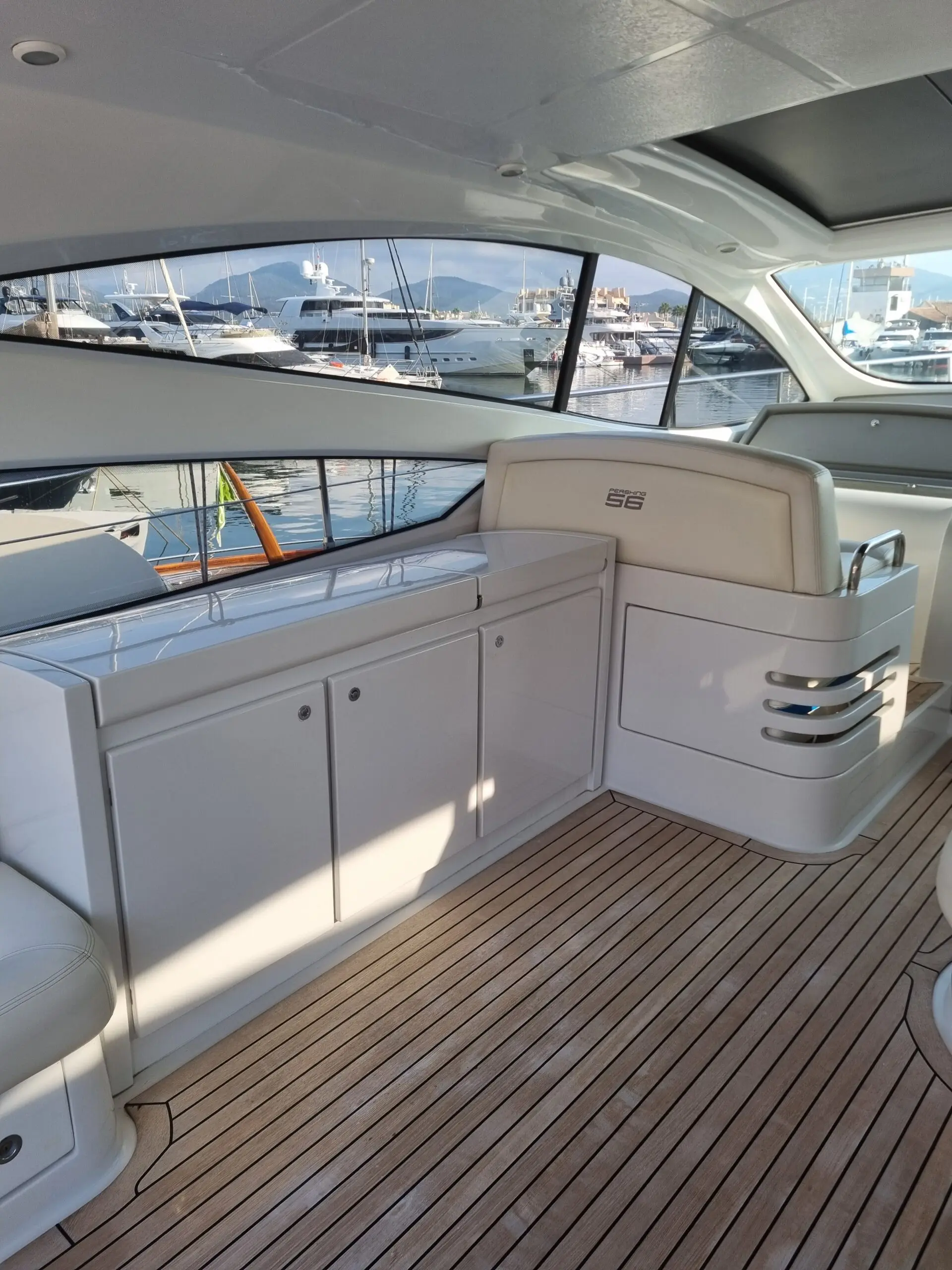 Pershing 56 HT — Vue du cockpit avec rangements, assise et pont en teck face à une marina.