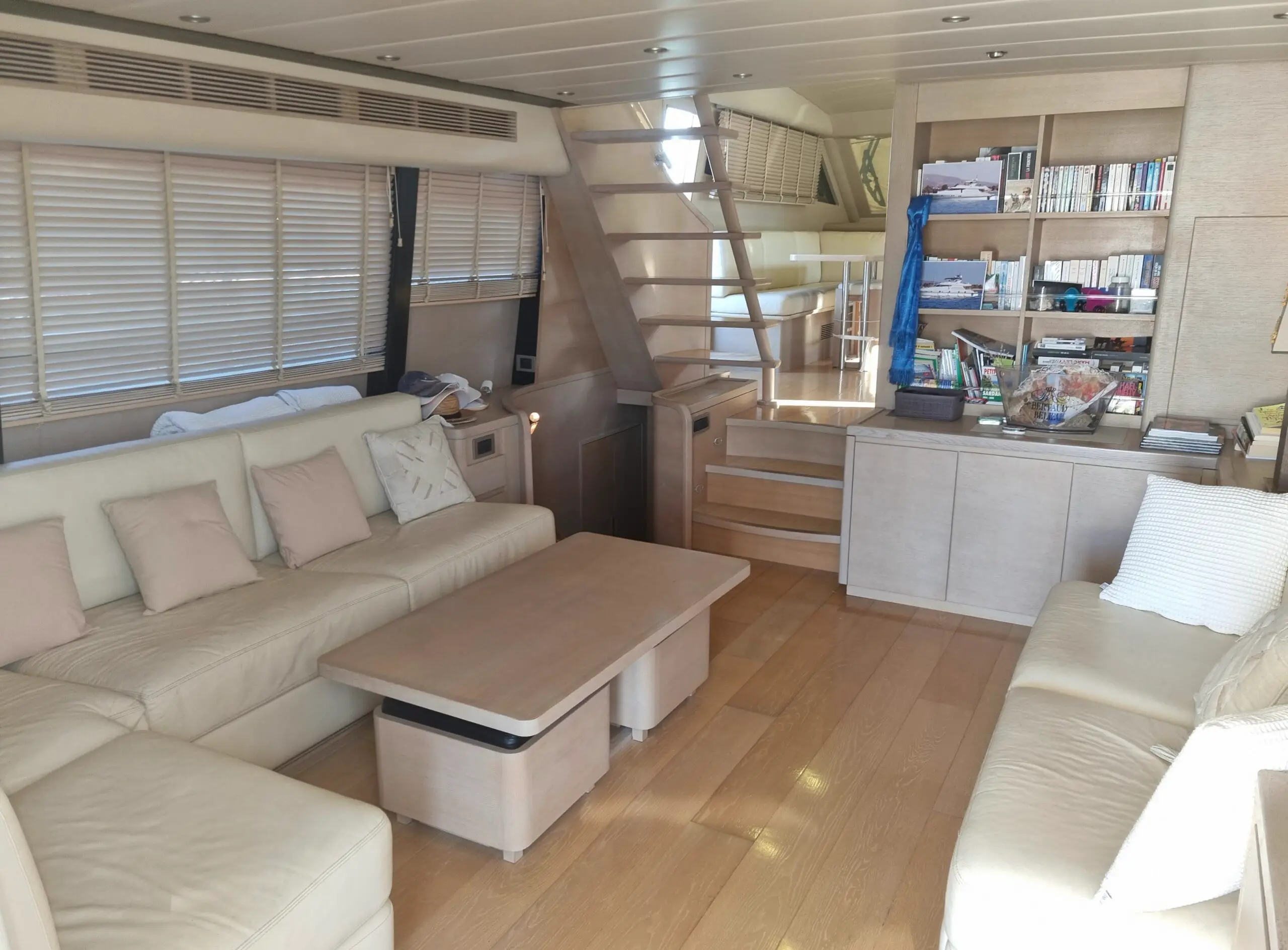 Guy Couach 2200 — Salon intérieur d’un bateau avec banquettes, table basse, escalier et bibliothèque.