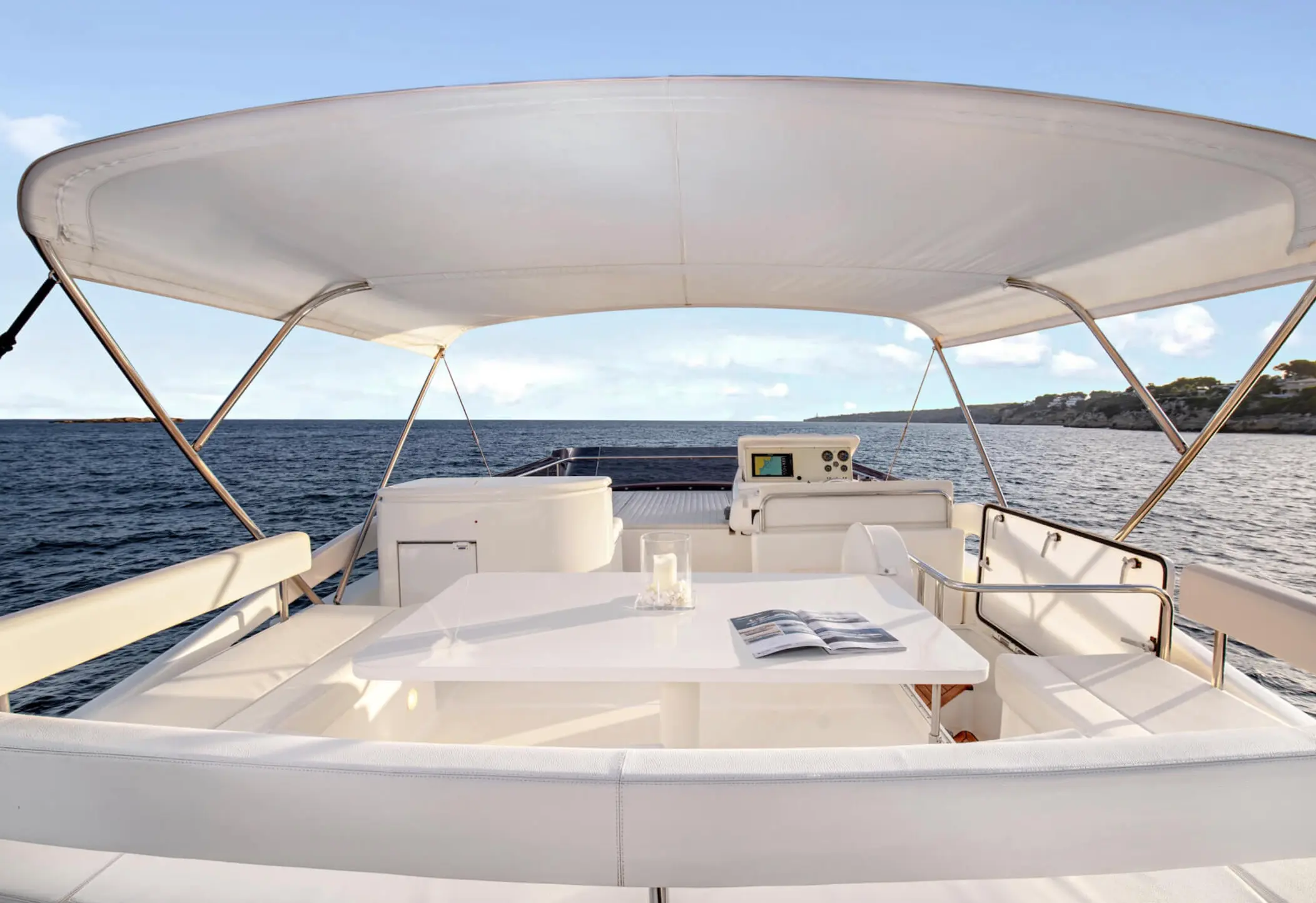 Ferretti 650 — Vue du cockpit arrière avec taud, table, sièges et poste de pilotage en mer.
