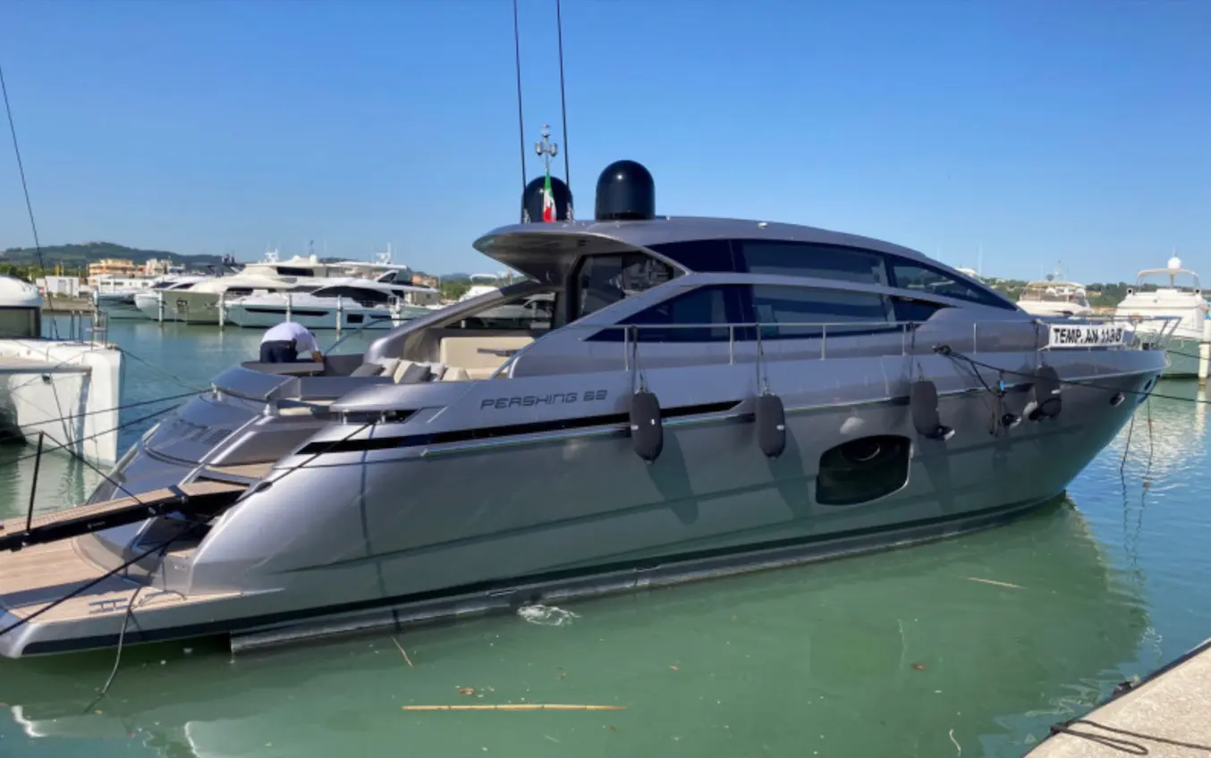 Pershing 62 — Vue tribord d’un yacht gris amarré dans une marina, avec d’autres bateaux en arrière-plan.