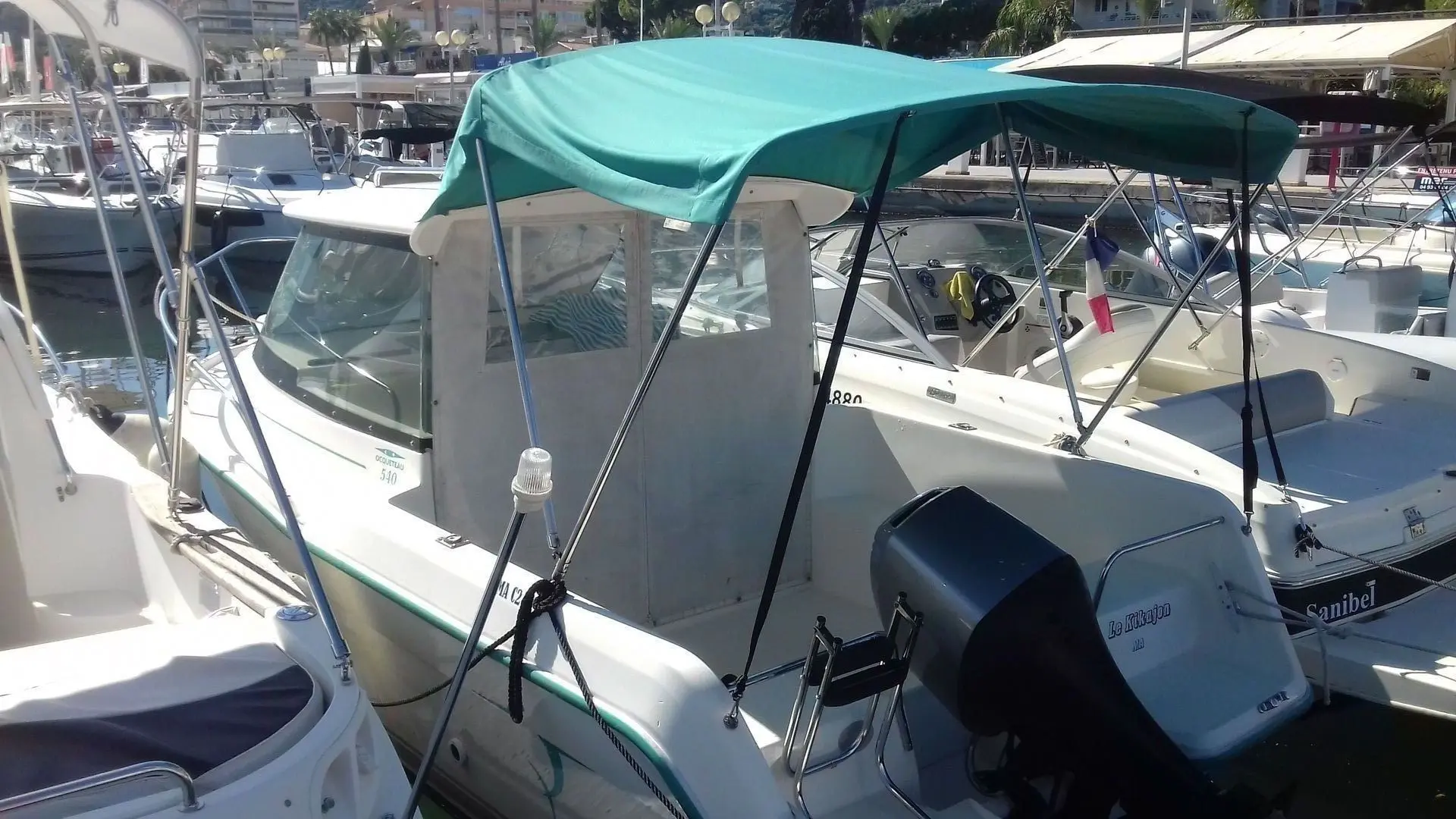 Ocqueteau 540 — Bateau à moteur amarré, équipé d’un taud turquoise et d’un moteur hors-bord.