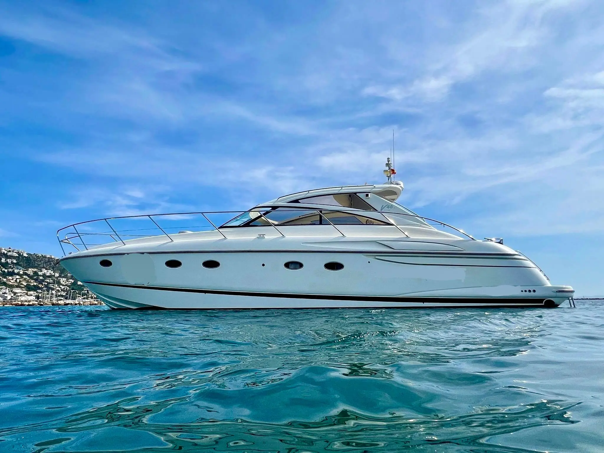 Princess V46 — Bateau à moteur blanc photographié de profil sur l’eau, devant une côte habitée.